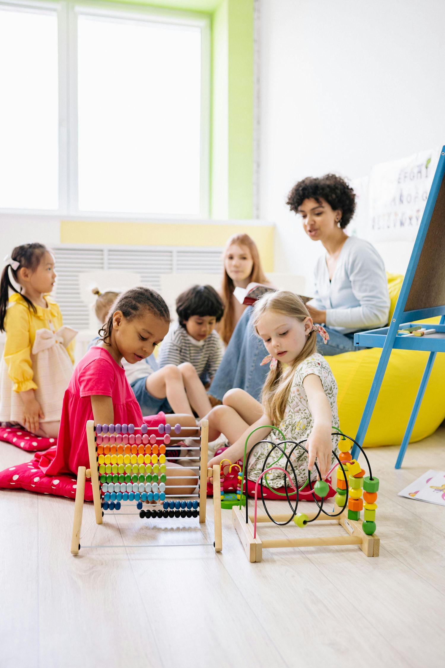 Children lying on floor using colorful abacus math tools in bright classroom with lime green window. Tempe Arizona.