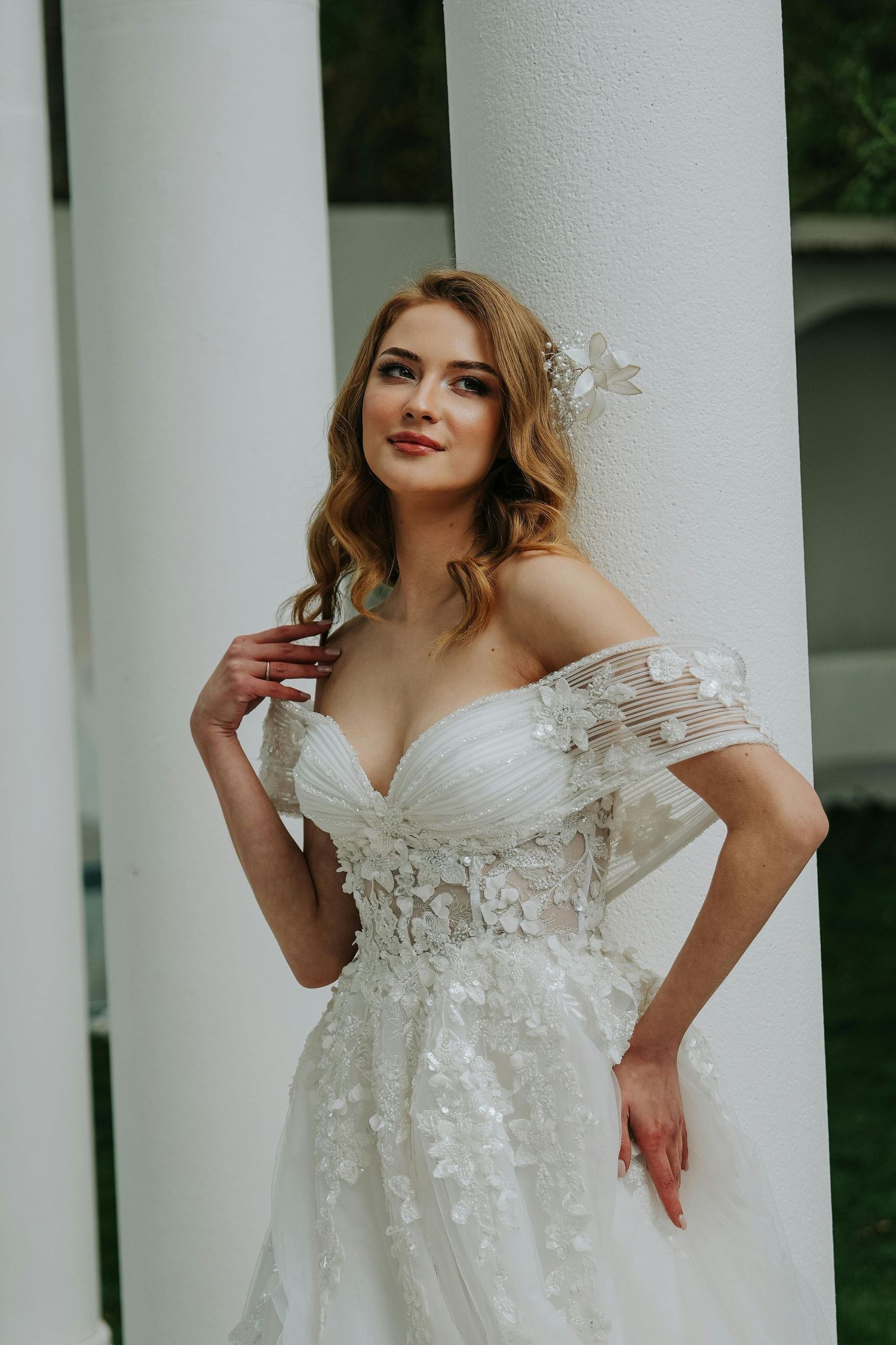 Elegant white wedding dress with delicate floral appliques photographed against classic white columns in outdoor setting. Top Photographer.