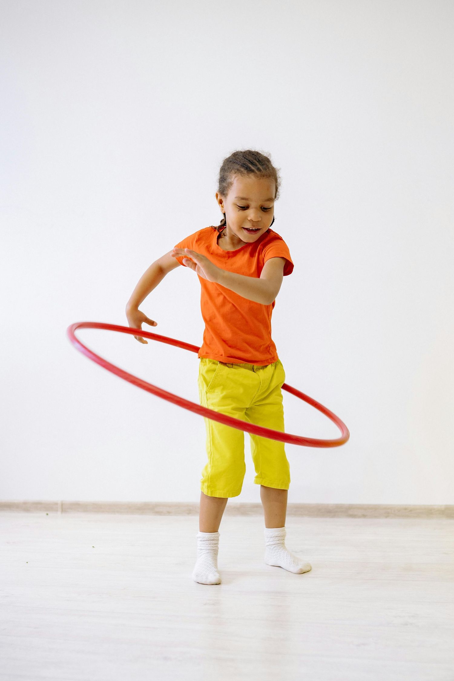 Queen Creek  Arizona Daycare Photography Child in orange shirt and yellow shorts practices hula hooping skills.