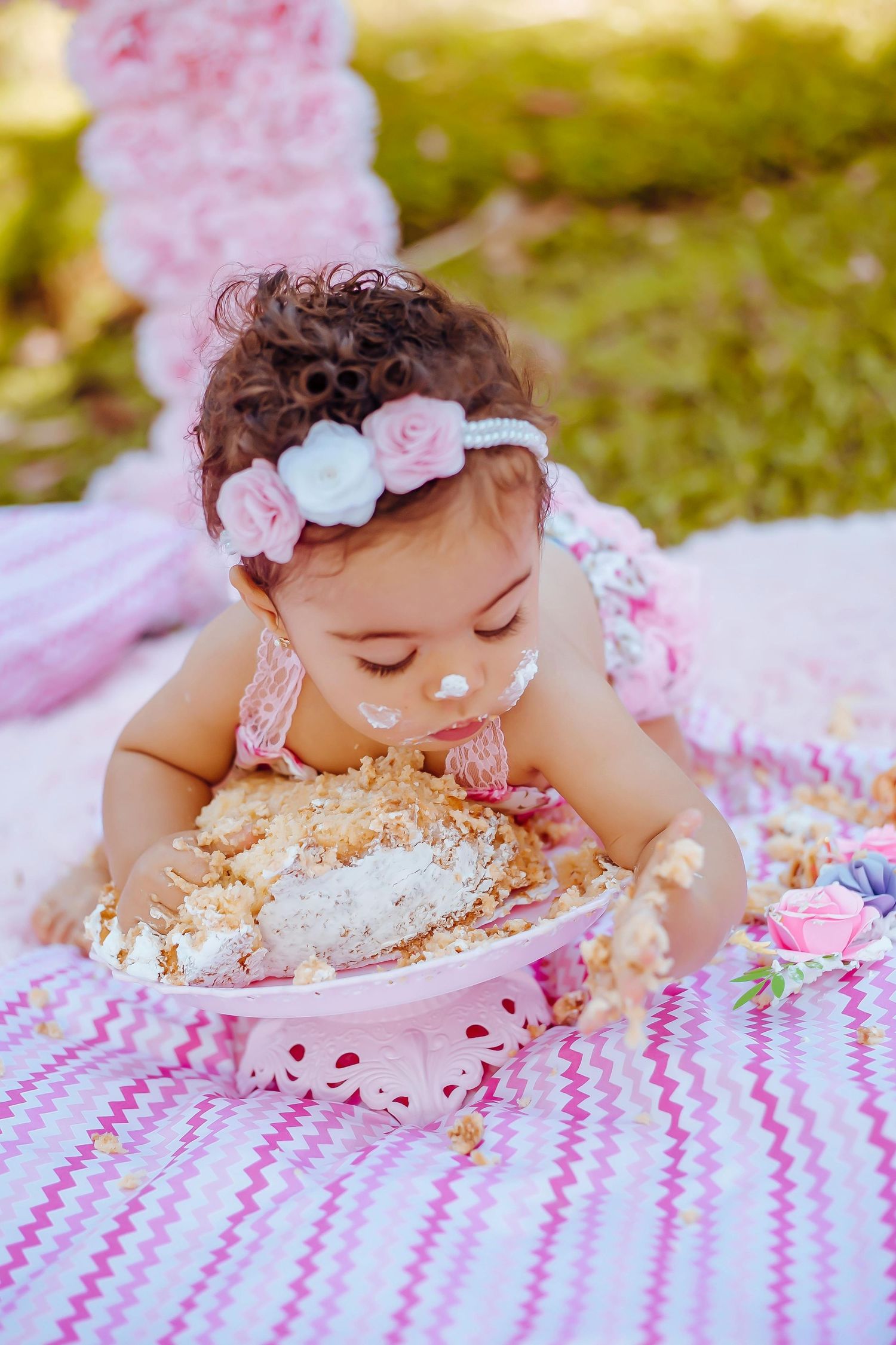 Baby enjoying a cake smash photo session with pink frosting and decorations on a chevron blanket outdoors. Anthem Arizona.