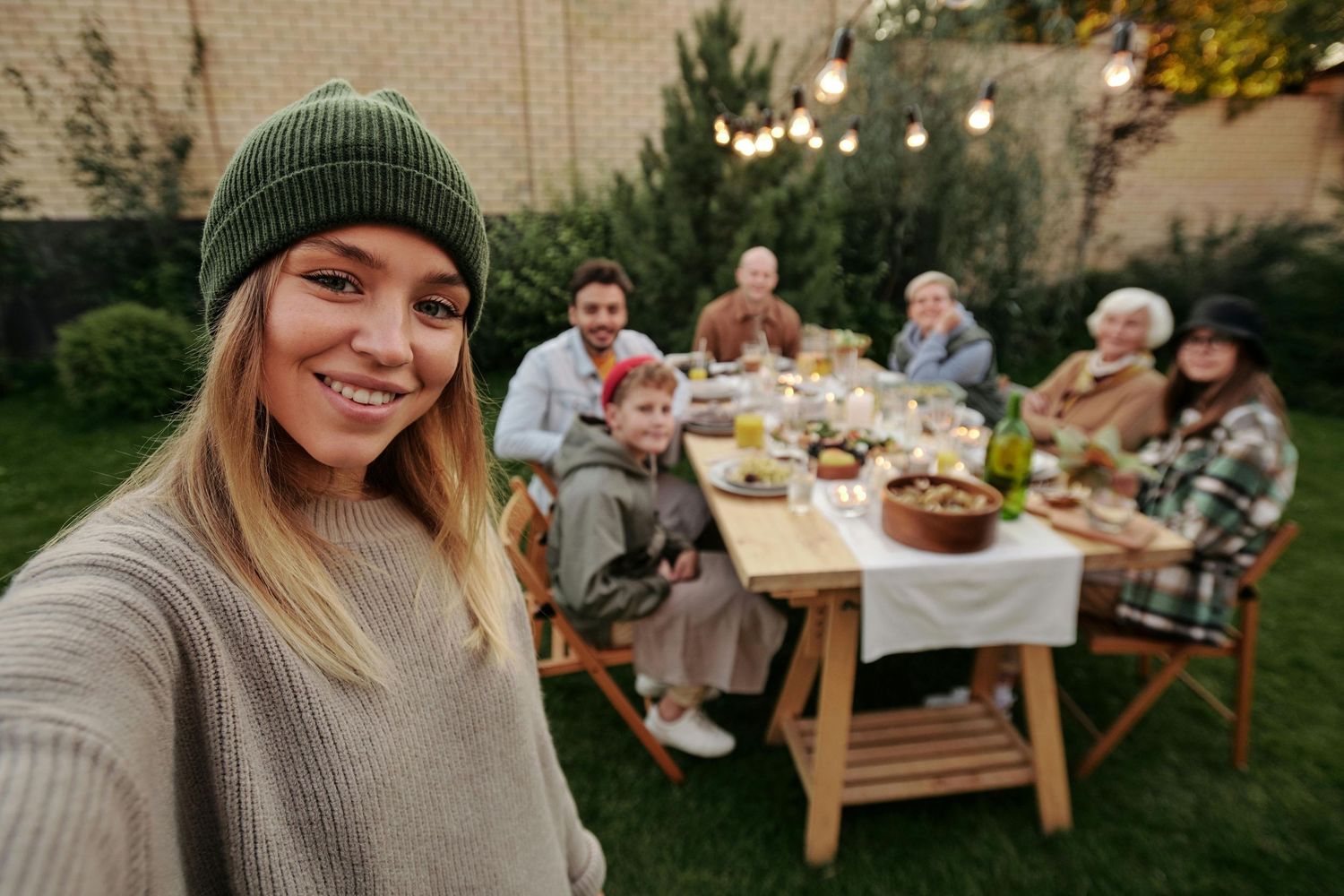 A family gathering around a wooden table for an outdoor meal in the backyard during autumn.