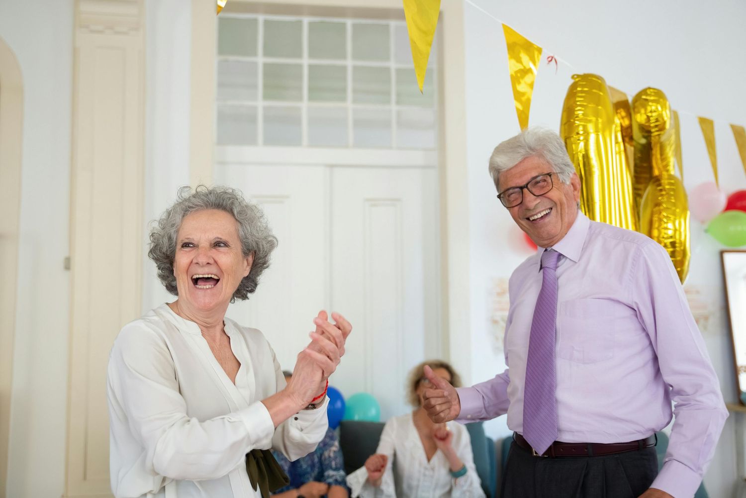Elderly people enjoying a social gathering with yellow decorations and party streamers in the background.
