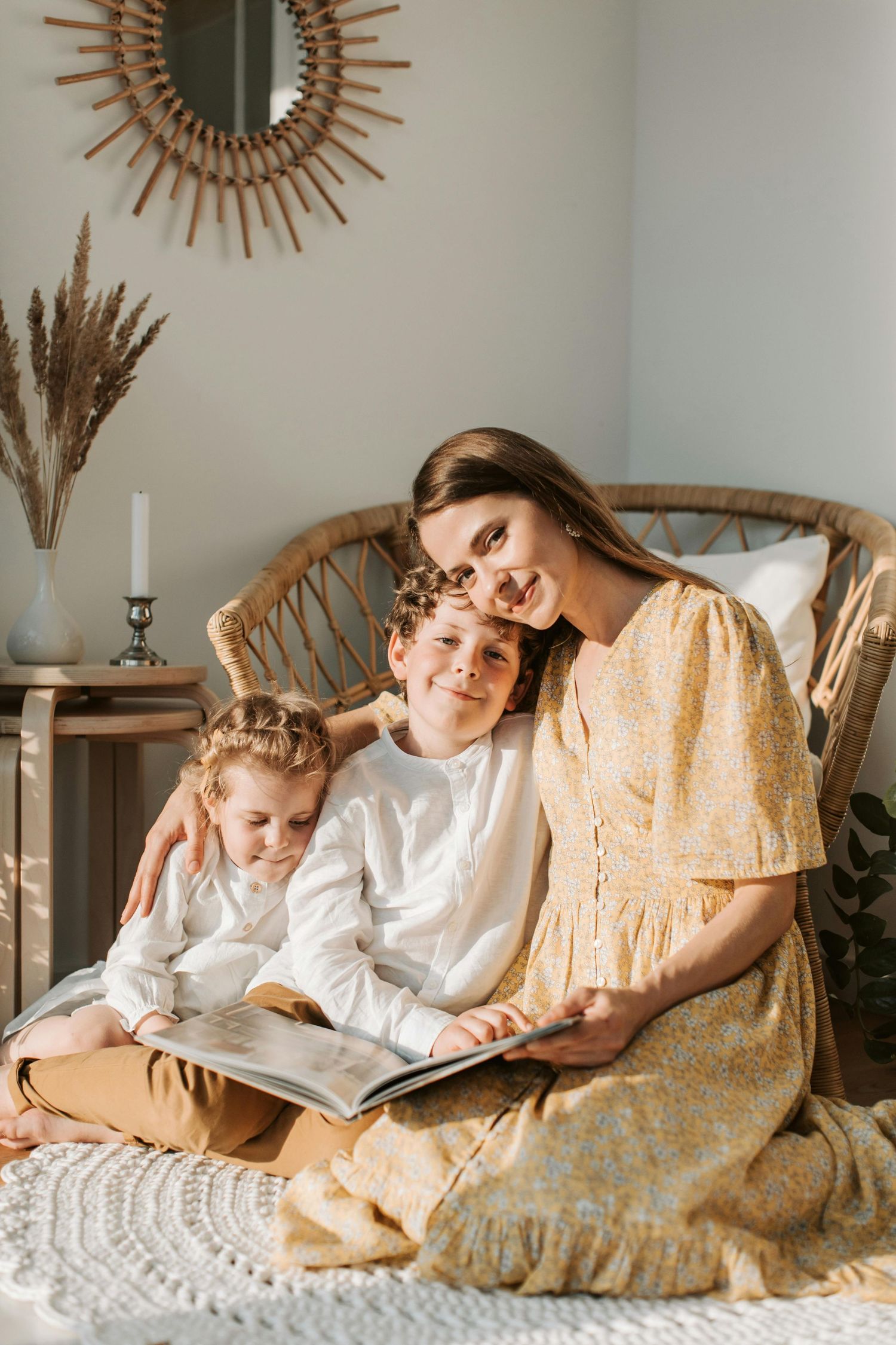 Cozy scene of reading together on a wicker chair with sunburst mirror and pampas grass decor in background.