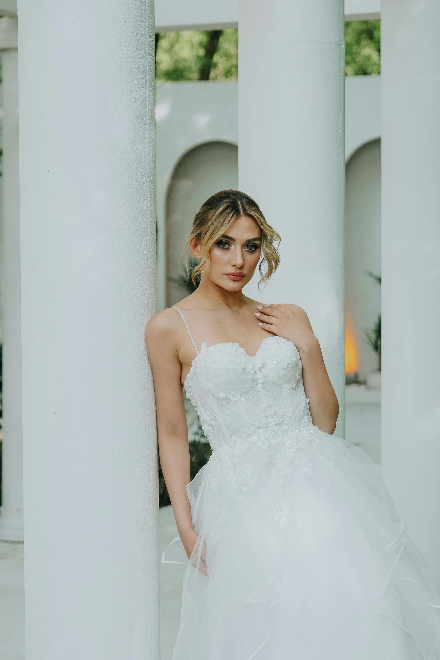 A bride in a white strapless wedding gown poses elegantly between classic white columns in an outdoor setting. Top Photographer Scottsdale.