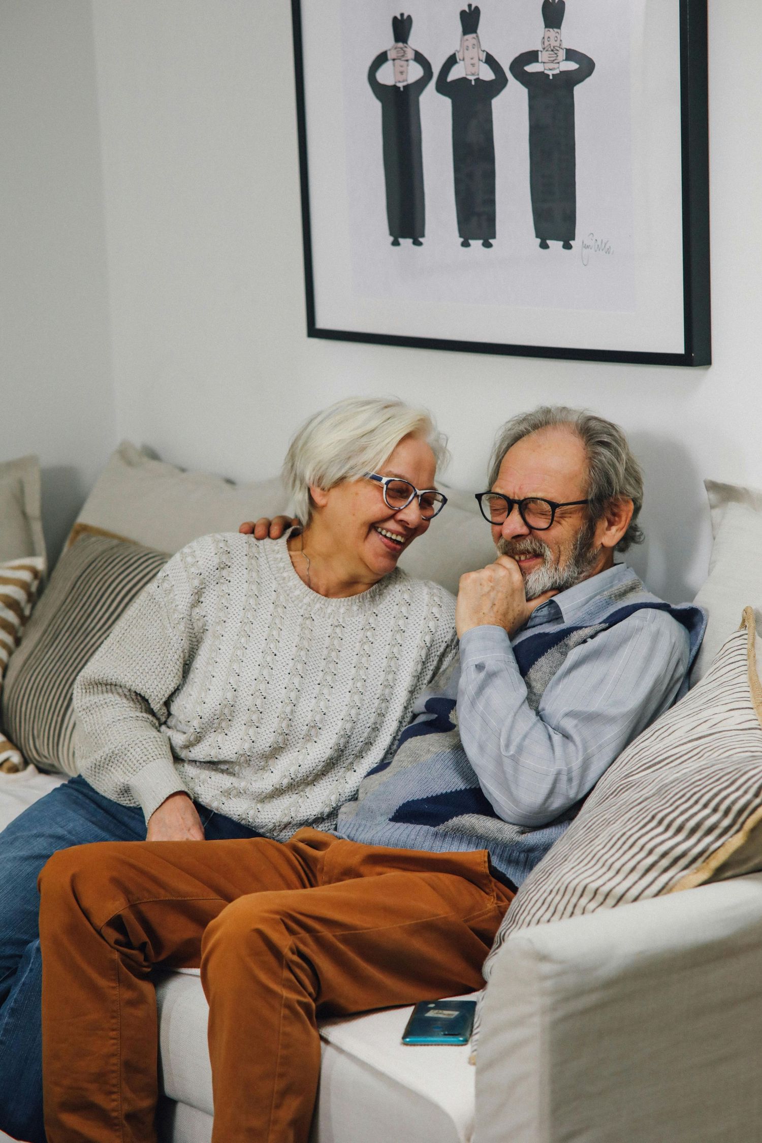 Elderly couple sharing a lighthearted moment while relaxing together on a comfortable gray couch.