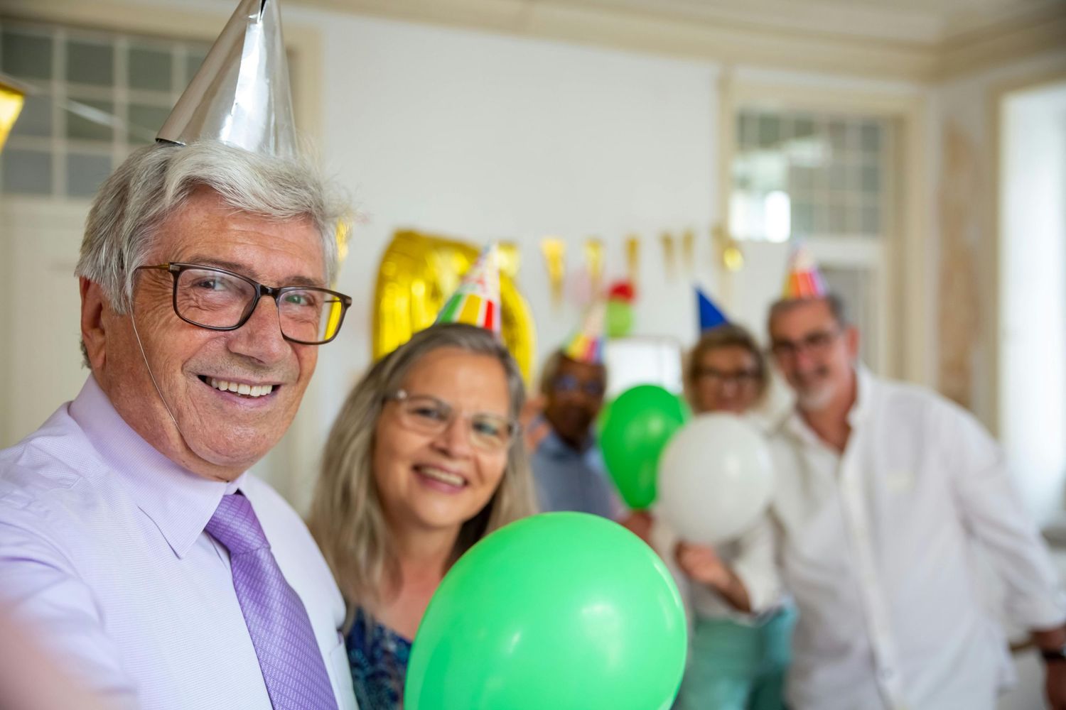 A festive party scene with colorful balloons and decorations as people gather to celebrate in a bright indoor space.