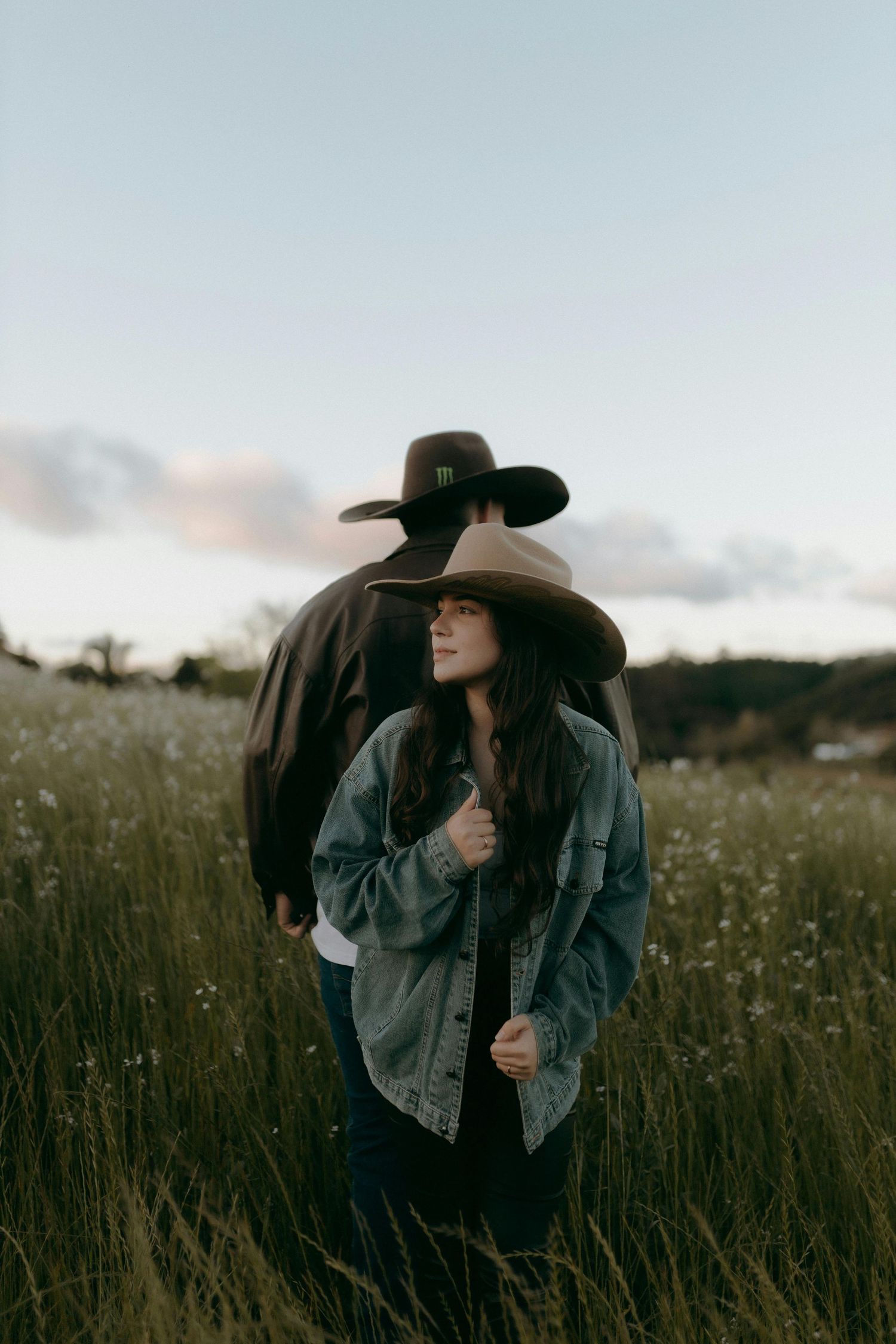 A person in a denim jacket and black cowboy hat stands thoughtfully in a wildflower meadow at dusk. Top Photographer Scottsdale.