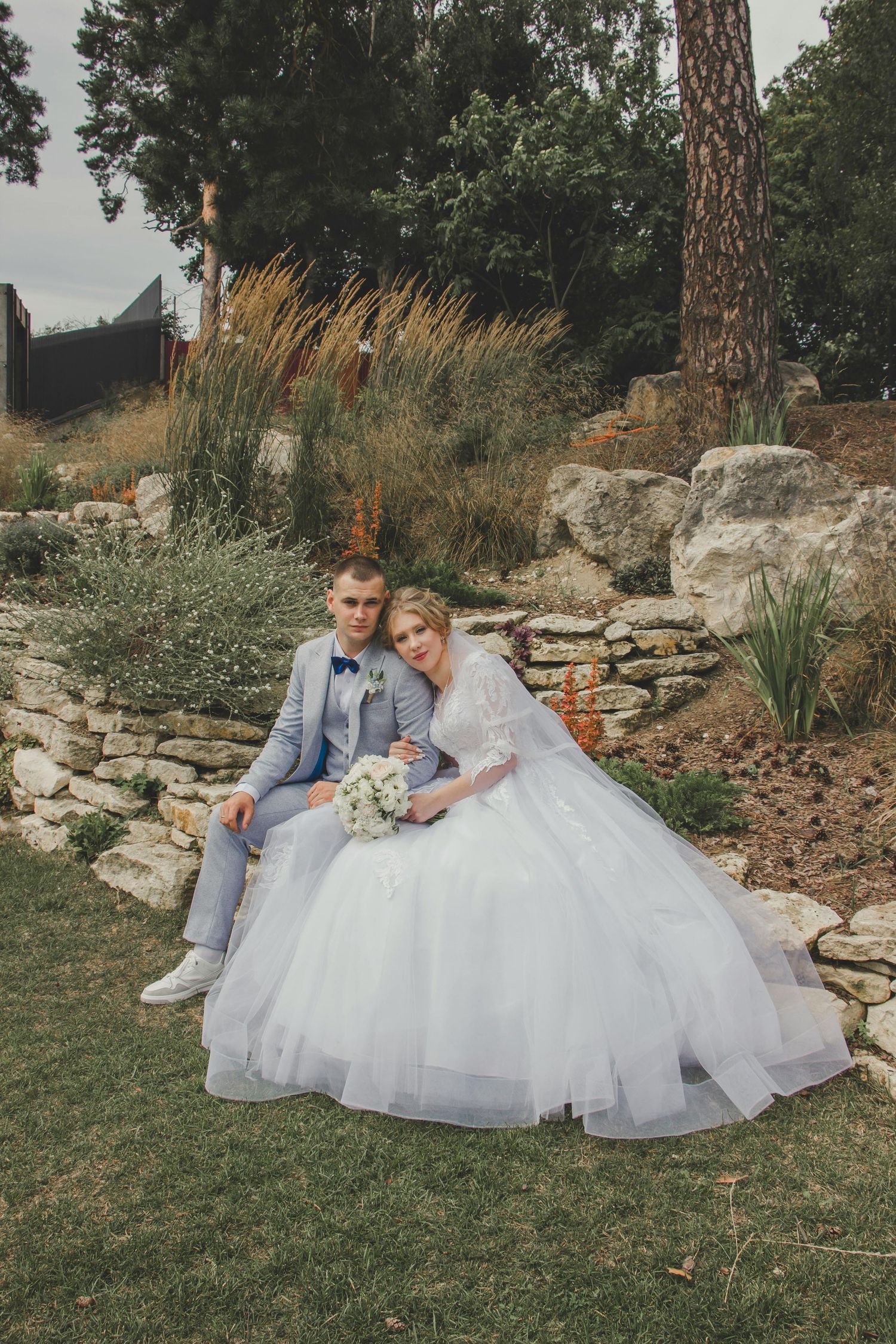 Outdoor wedding portraits with a couple posing on a rustic stone wall surrounded by natural landscape. Trusted Sedona Photographer.