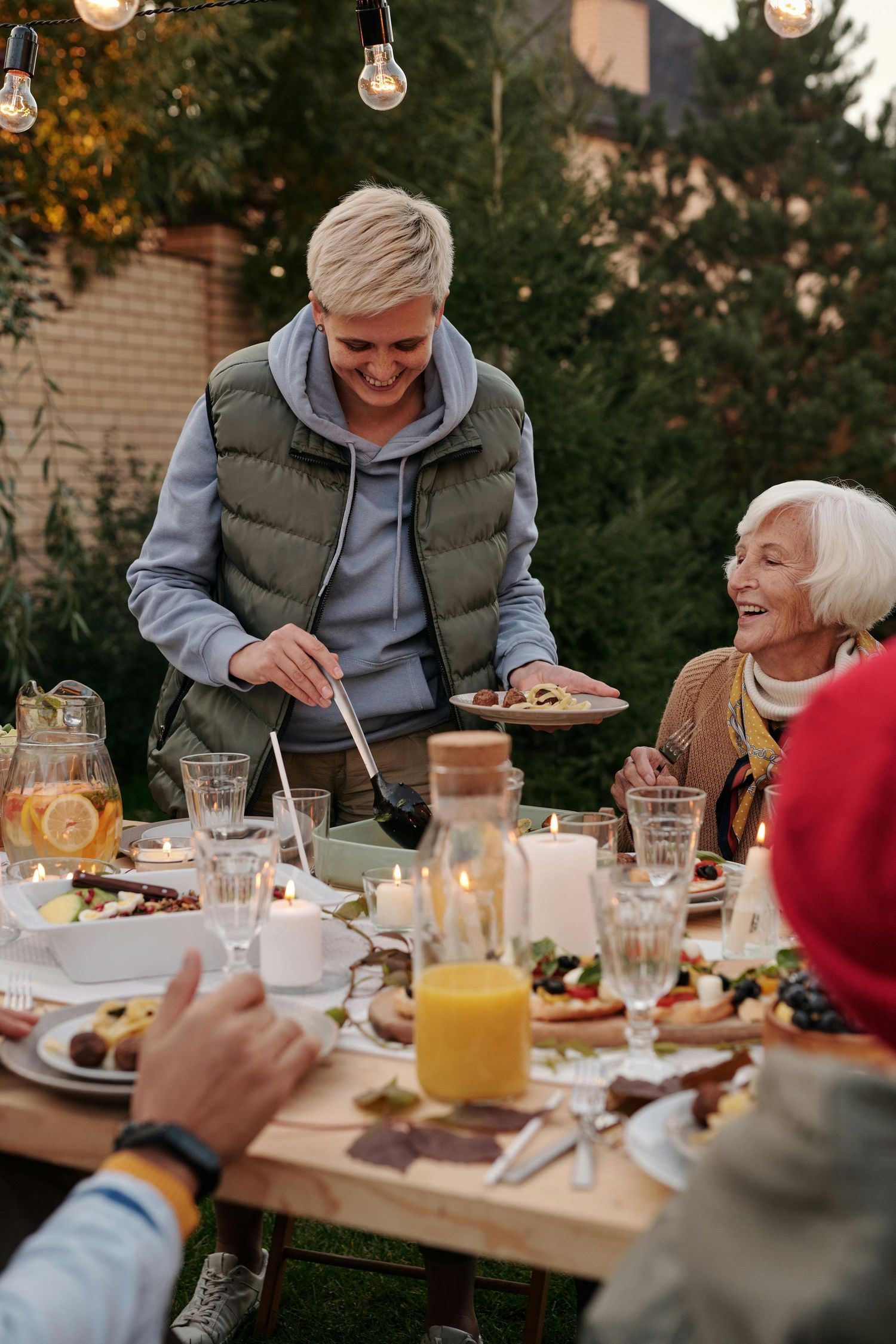 People enjoying a festive outdoor dinner gathering with drinks and food at a long table.