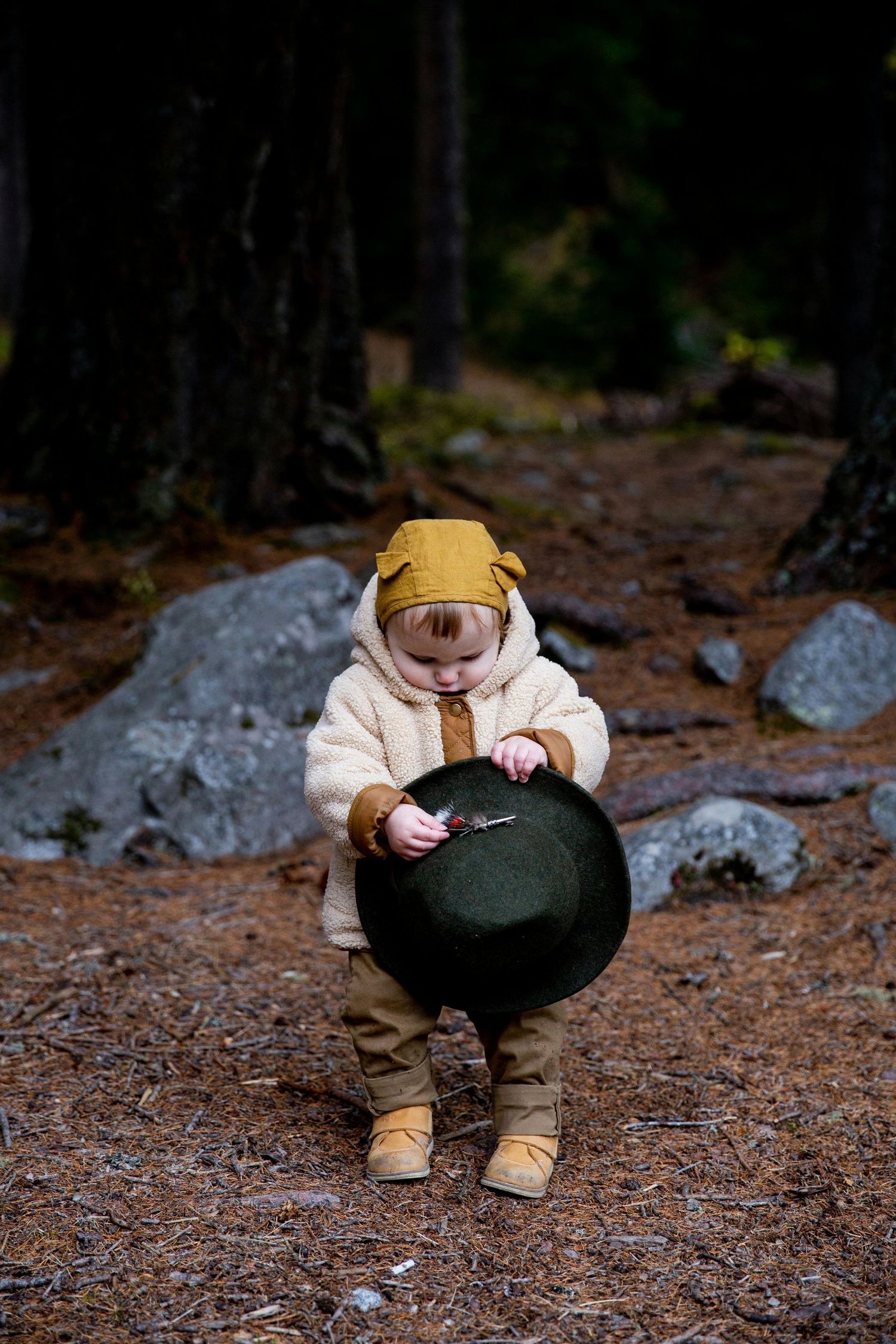 Sedona Arizona Portraits Small figure in beige clothing and cap sits on forest ground examining something.