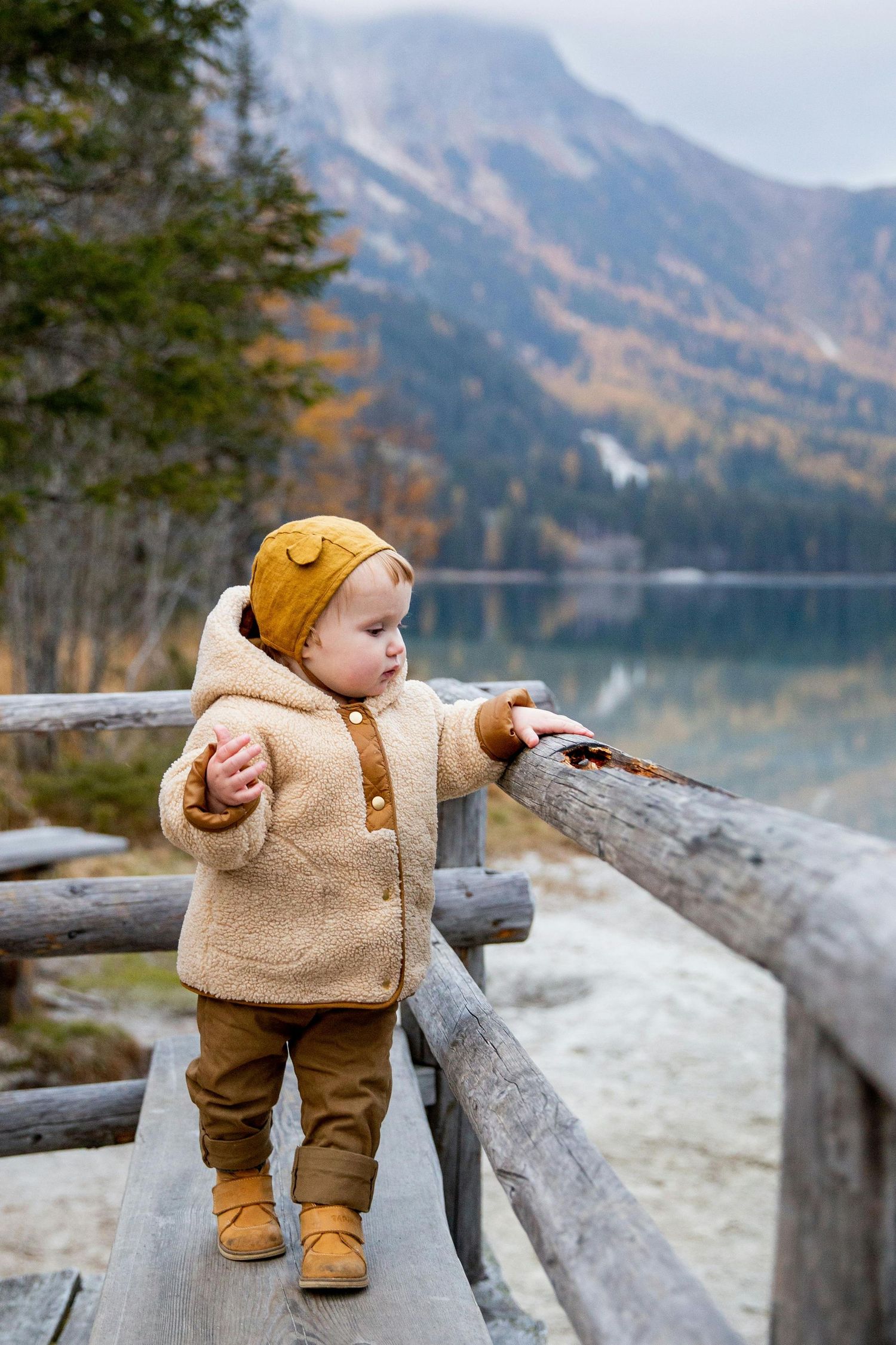 Sedona Arizona Portraits Small figure in cozy beige outfit explores wooden railing by mountain lake.