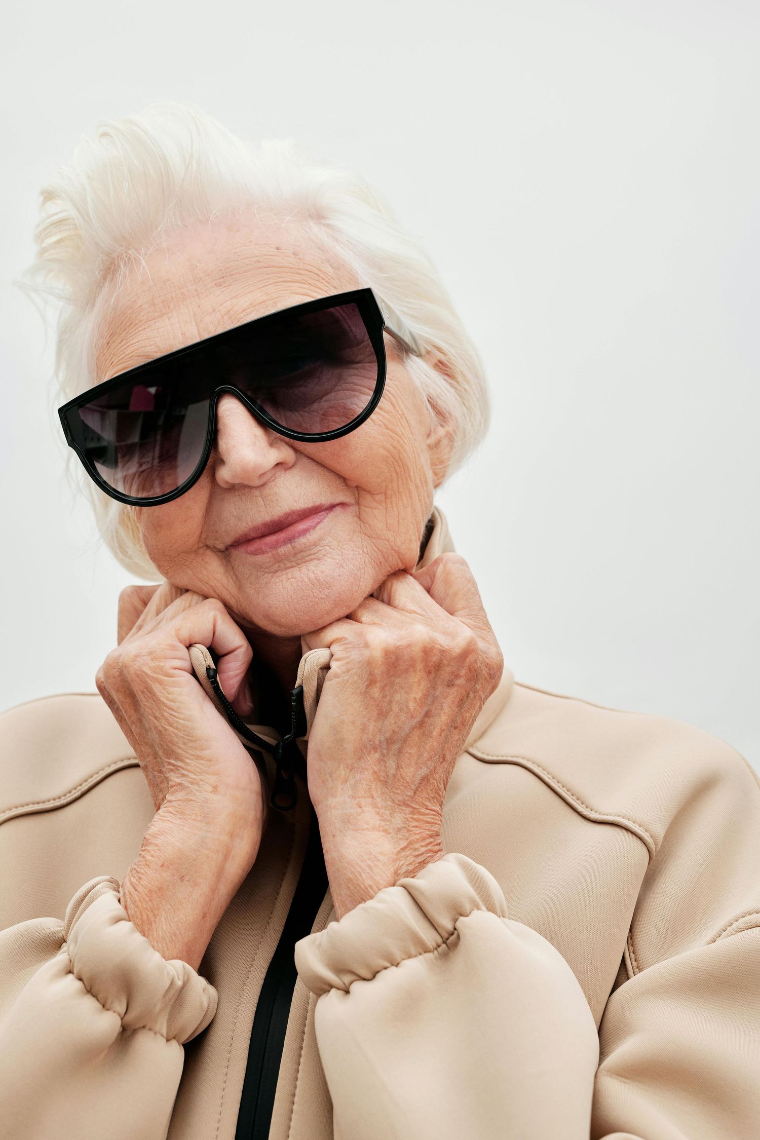 An elderly person wearing sunglasses and a beige jacket poses playfully in a four-part photo series.