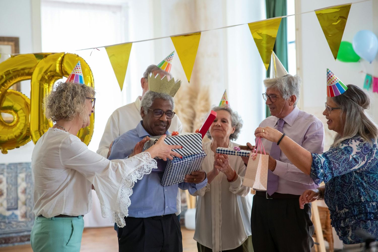 Elderly people dancing and socializing at a party decorated with yellow and green bunting flags.