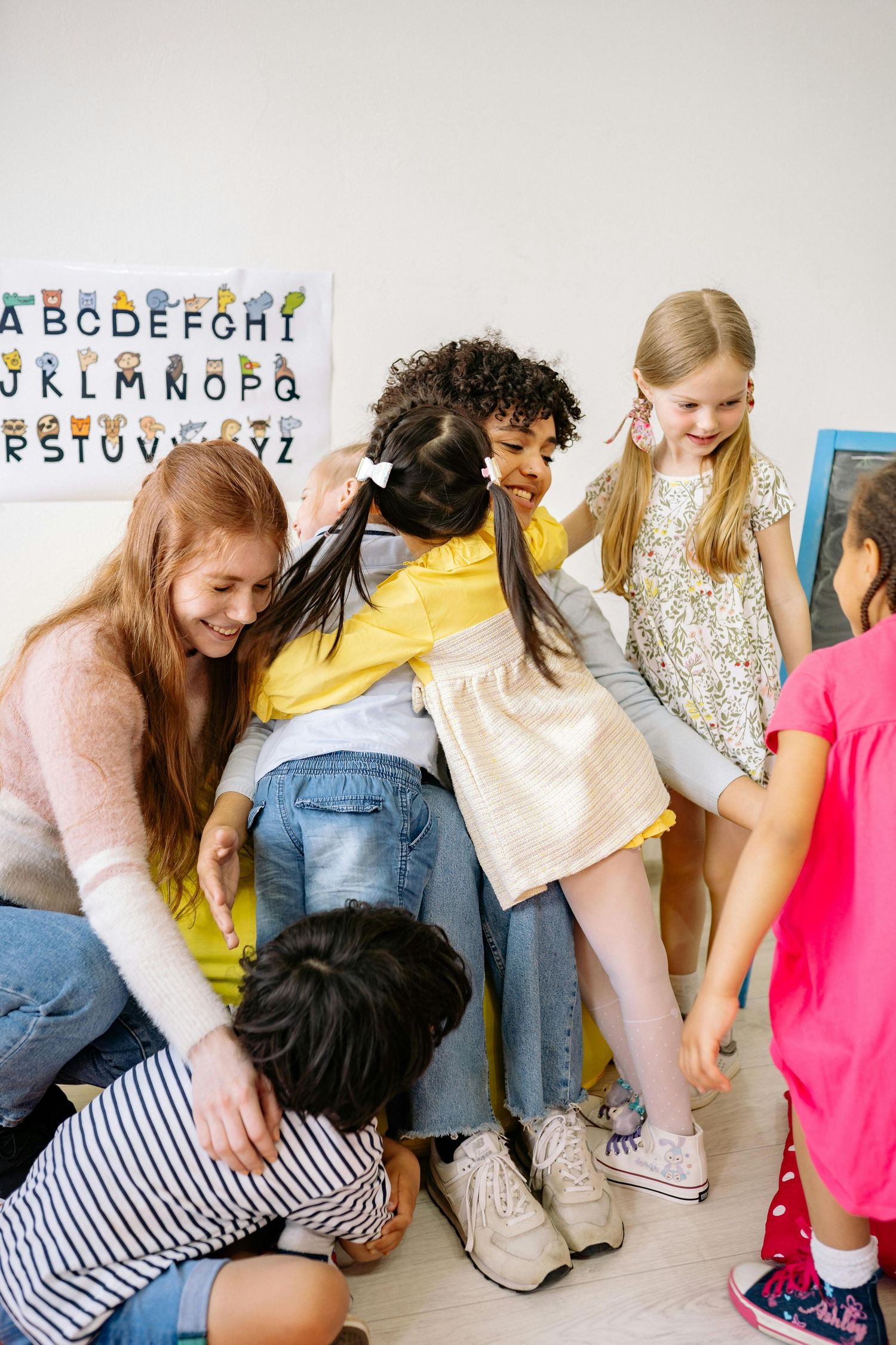 Group of children petting and interacting with a black dog in a classroom setting with alphabet letters on the wall. Phoenix Arizona.