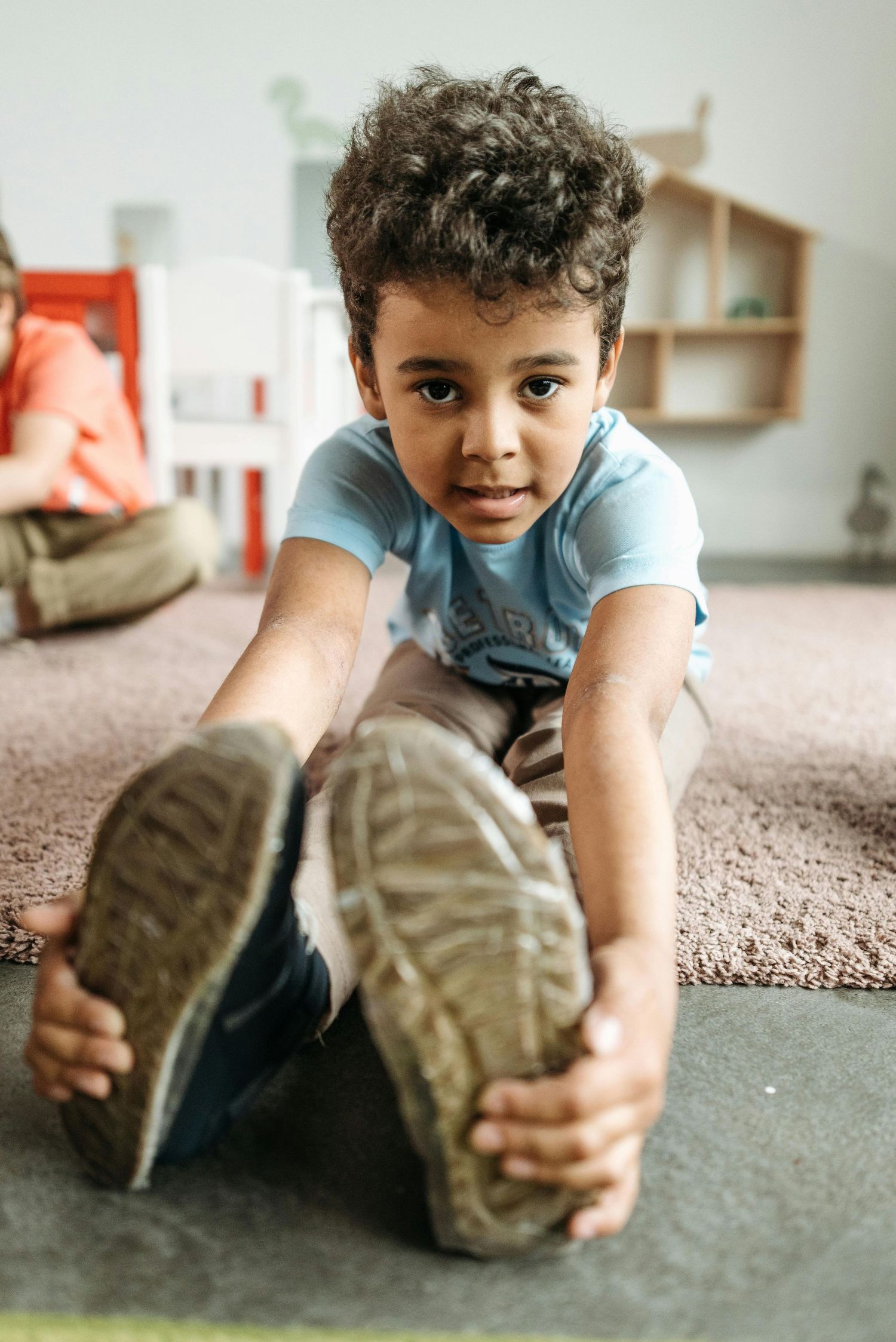 Arizona Daycare Photography Young child in light blue shirt playing and stretching on a carpeted floor.