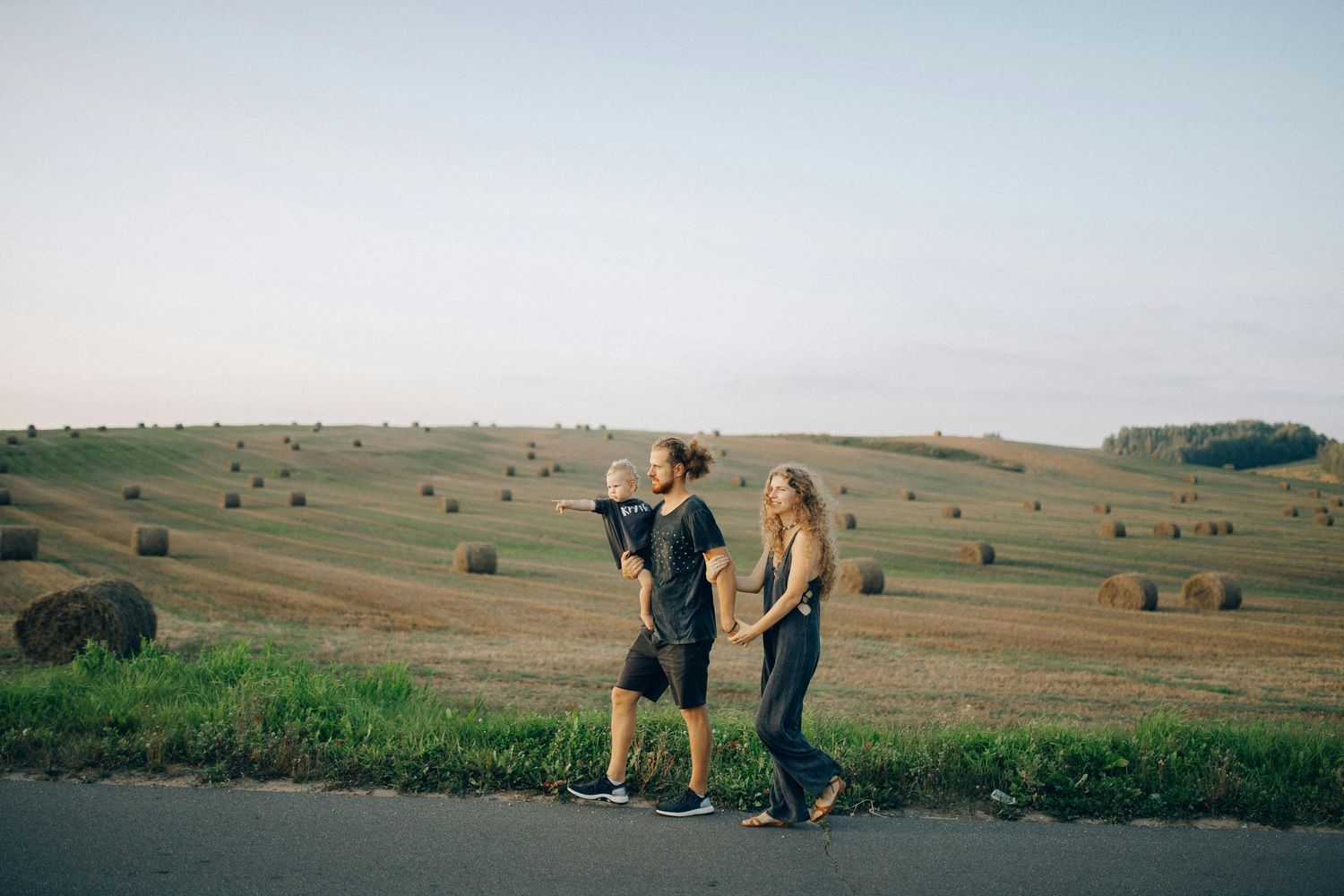Two people walking together on a path overlooking rolling hills dotted with hay bales.
