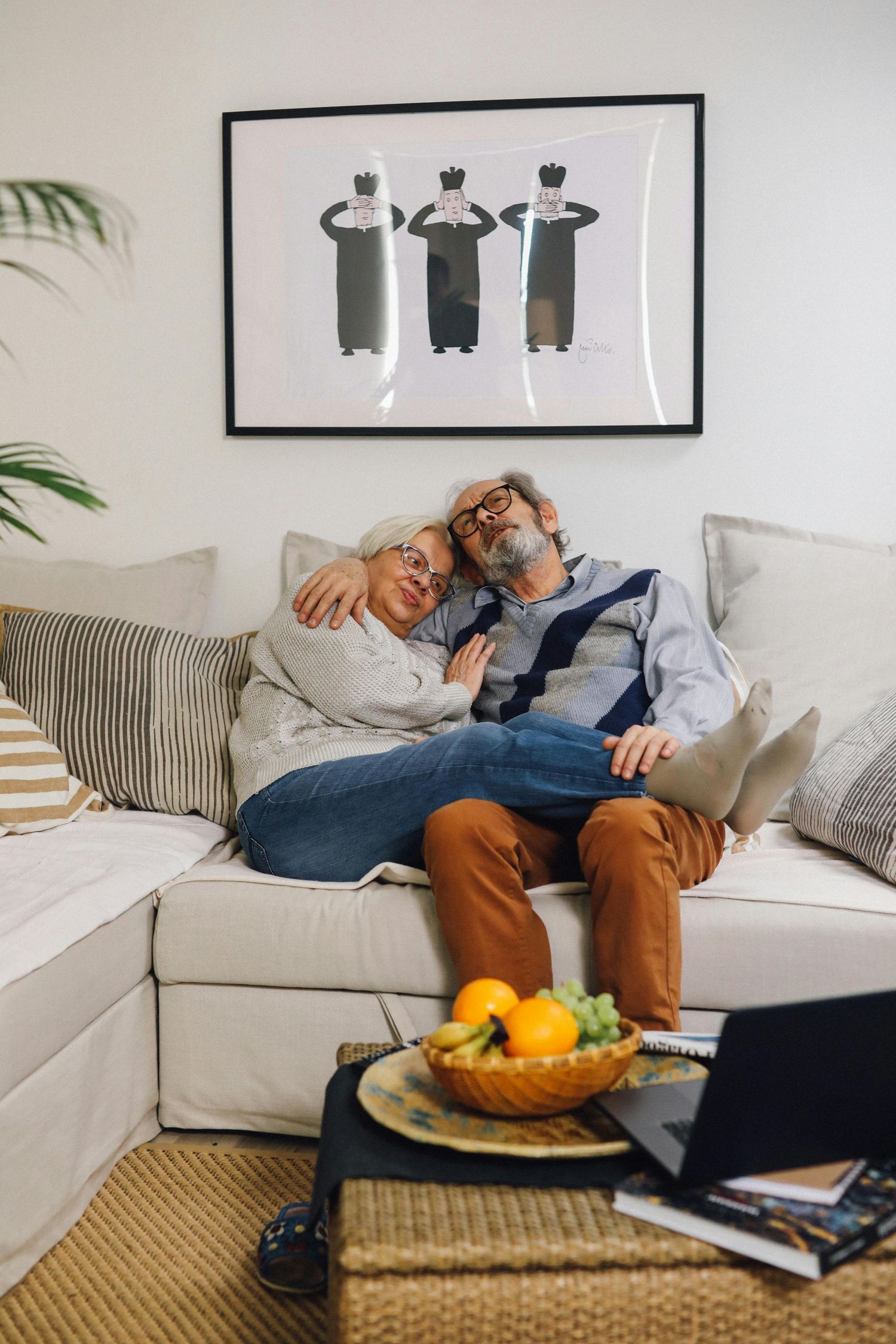 Person napping on a white couch with laptop nearby and decorative throw pillows in a modern living room setting.