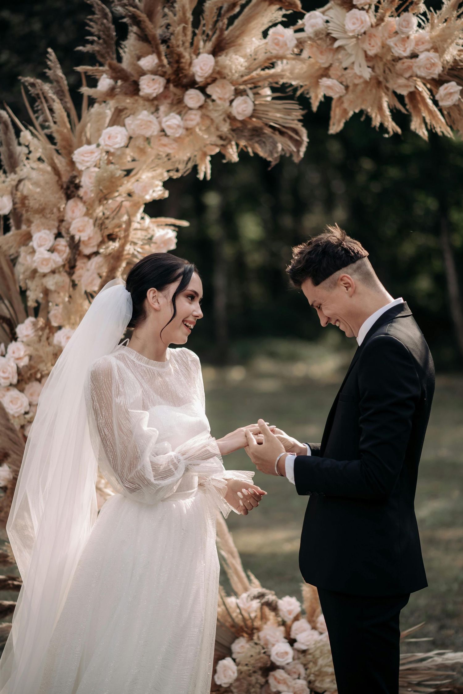 A bride and groom exchange rings during their wedding ceremony beneath an elegant floral arch. Top Photographer Scottsdale.