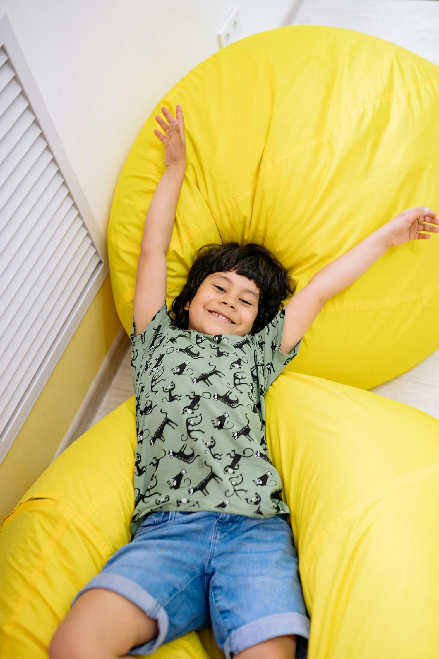 Queen Creek  Arizona Daycare Photography Child relaxing on a bright yellow bean bag chair in a classroom setting.
