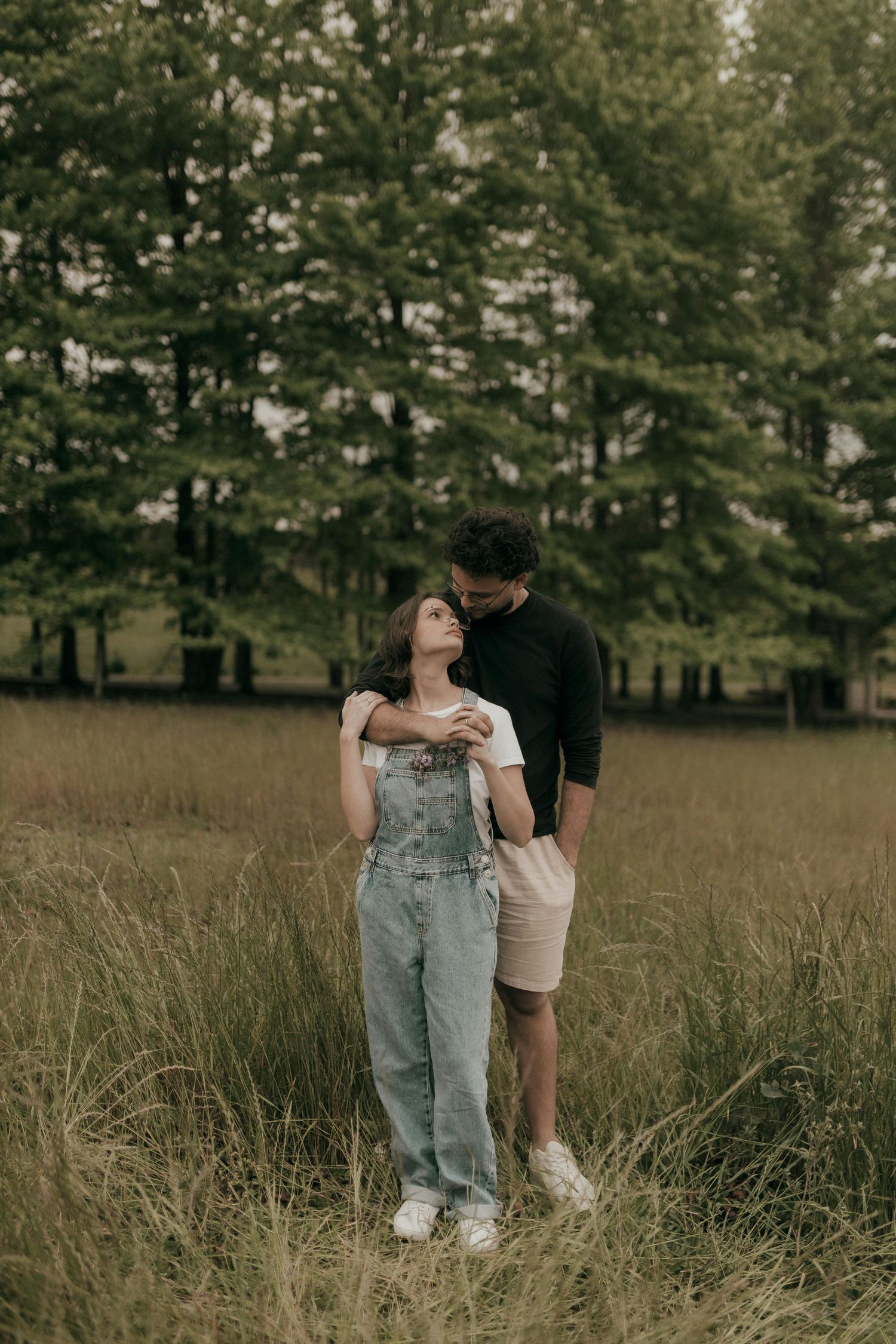 A couple stands together in a golden field surrounded by tall grass and trees on an autumn afternoon. Best Photographer Phoenix.