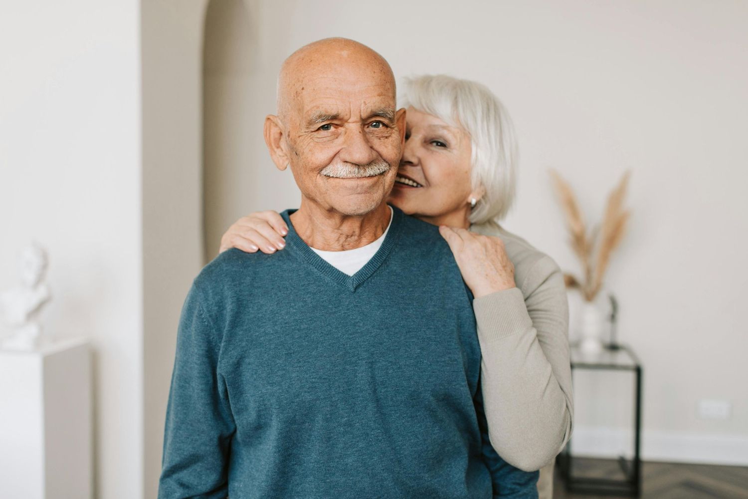 Tender moment between two people against white wall with minimal decor.