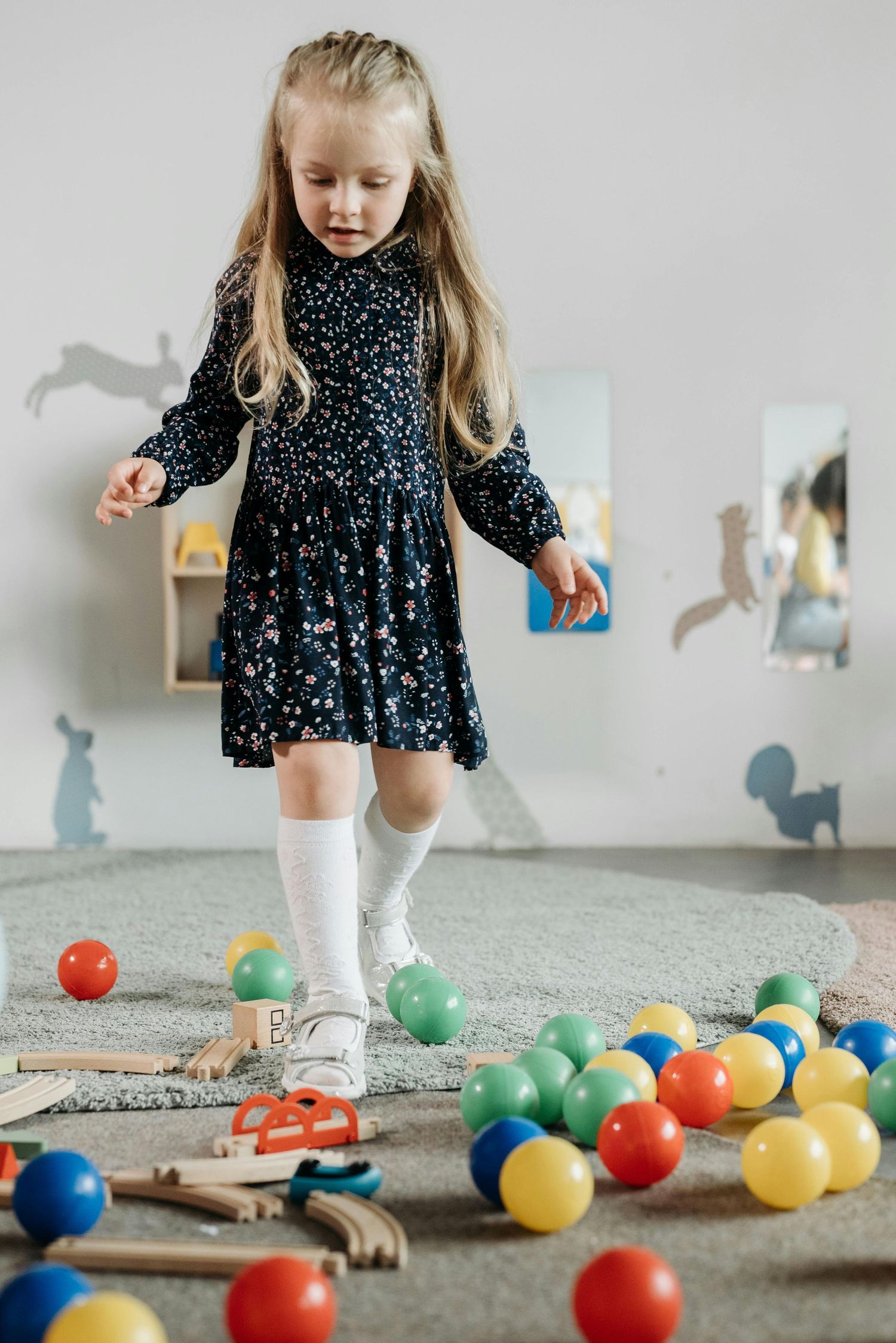 Scottsdale Arizona Photography Child in polka dot dress playing with colorful balls scattered on gray carpet.