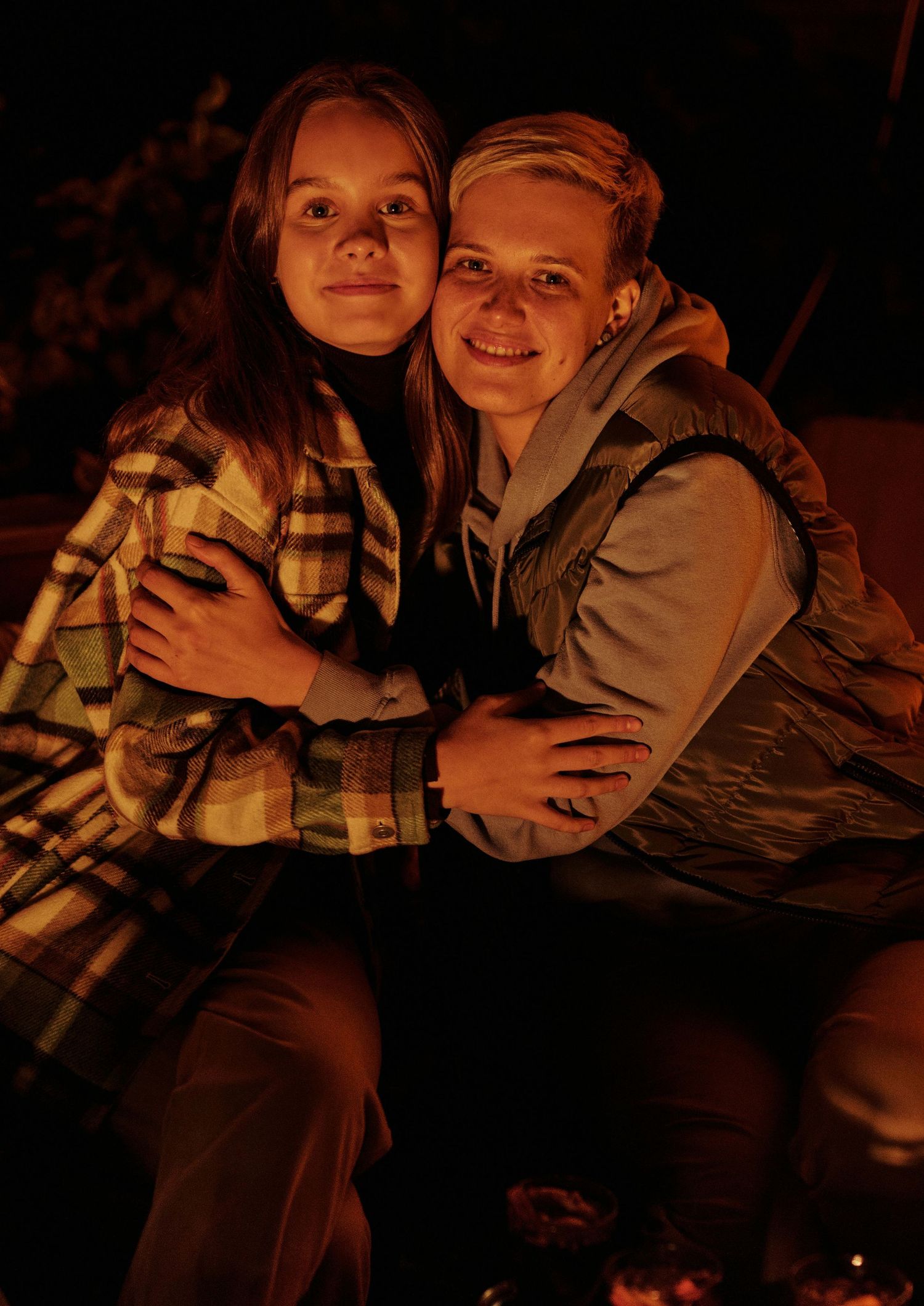 Two people share a warm embrace while sitting together in warm firelight.