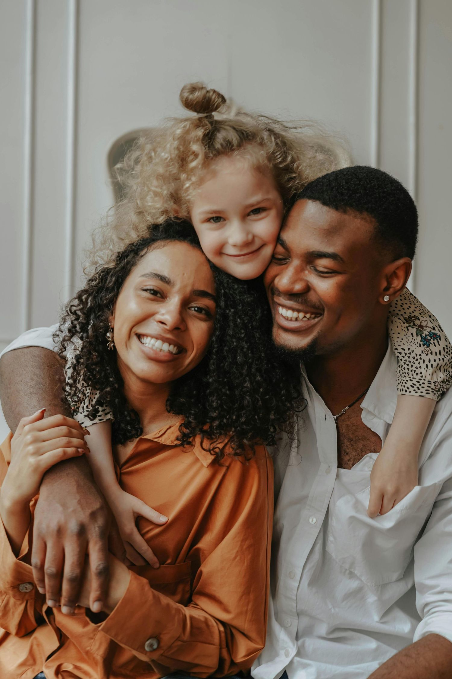 Family Studio Photography Sedona. A happy family of three laughs and embraces while sitting together against a white wall.