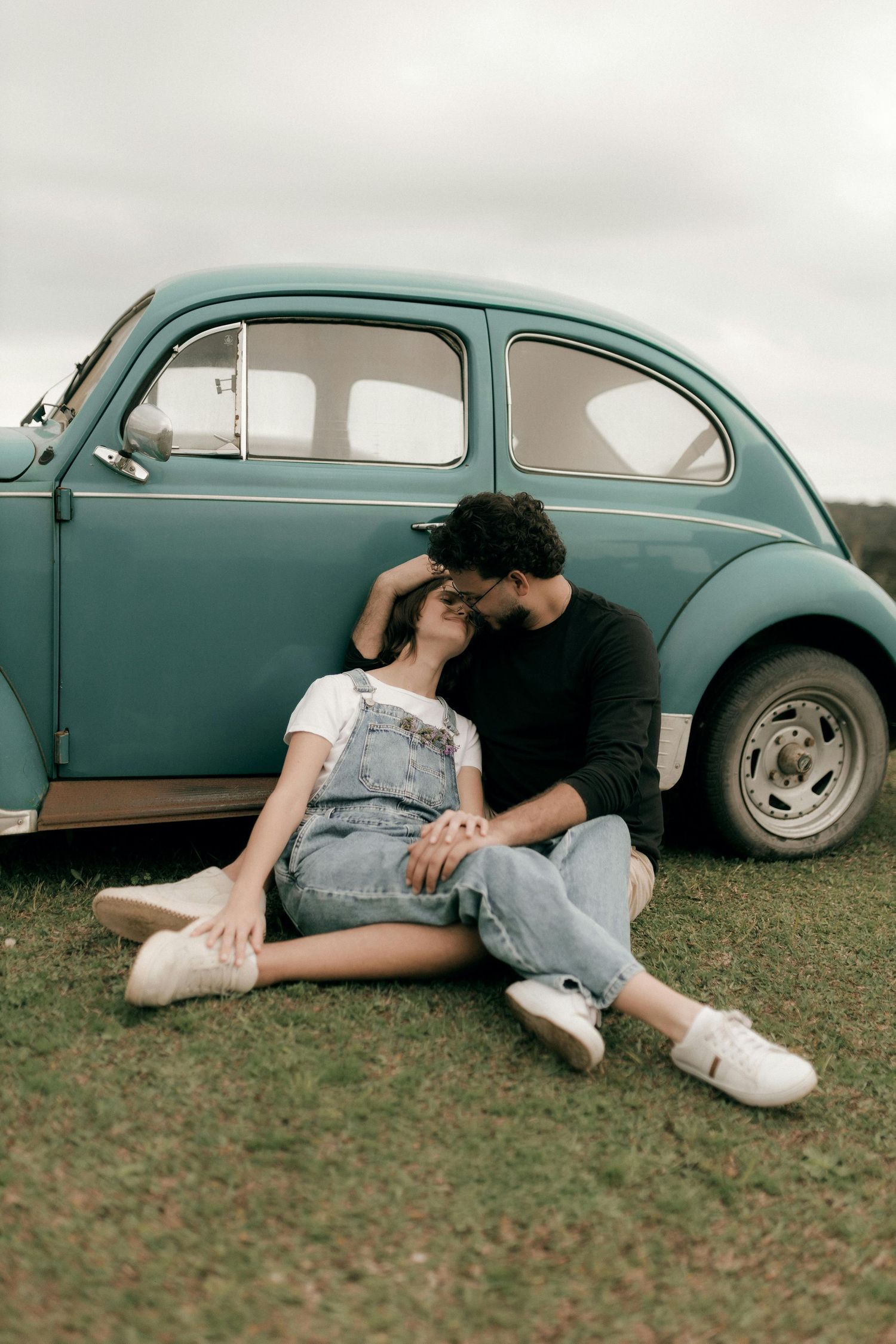 Scottsdale Arizona Photography Couple cuddling against vintage teal Volkswagen Beetle on grassy field.