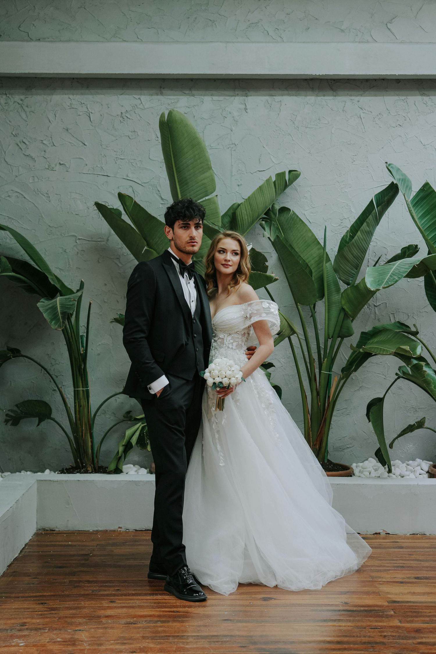 A romantic wedding photo series showing a couple posing against a white wall with large tropical plants.  Award Winning Photographer Gilbert