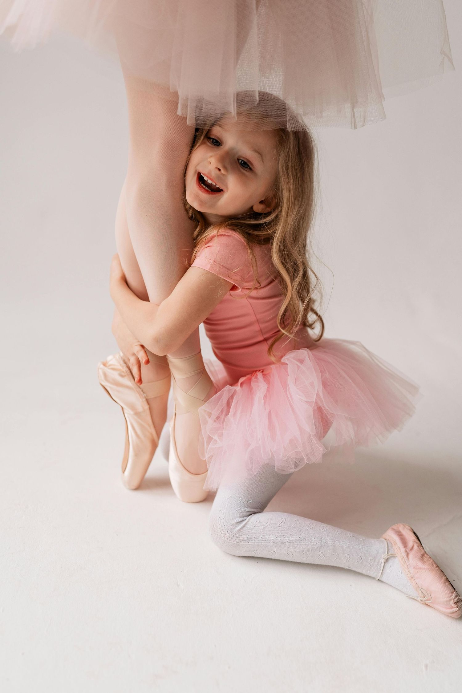 Studio portraits arizona. A ballet dancer in a pink tutu and leotard stretches gracefully on a light-colored floor.