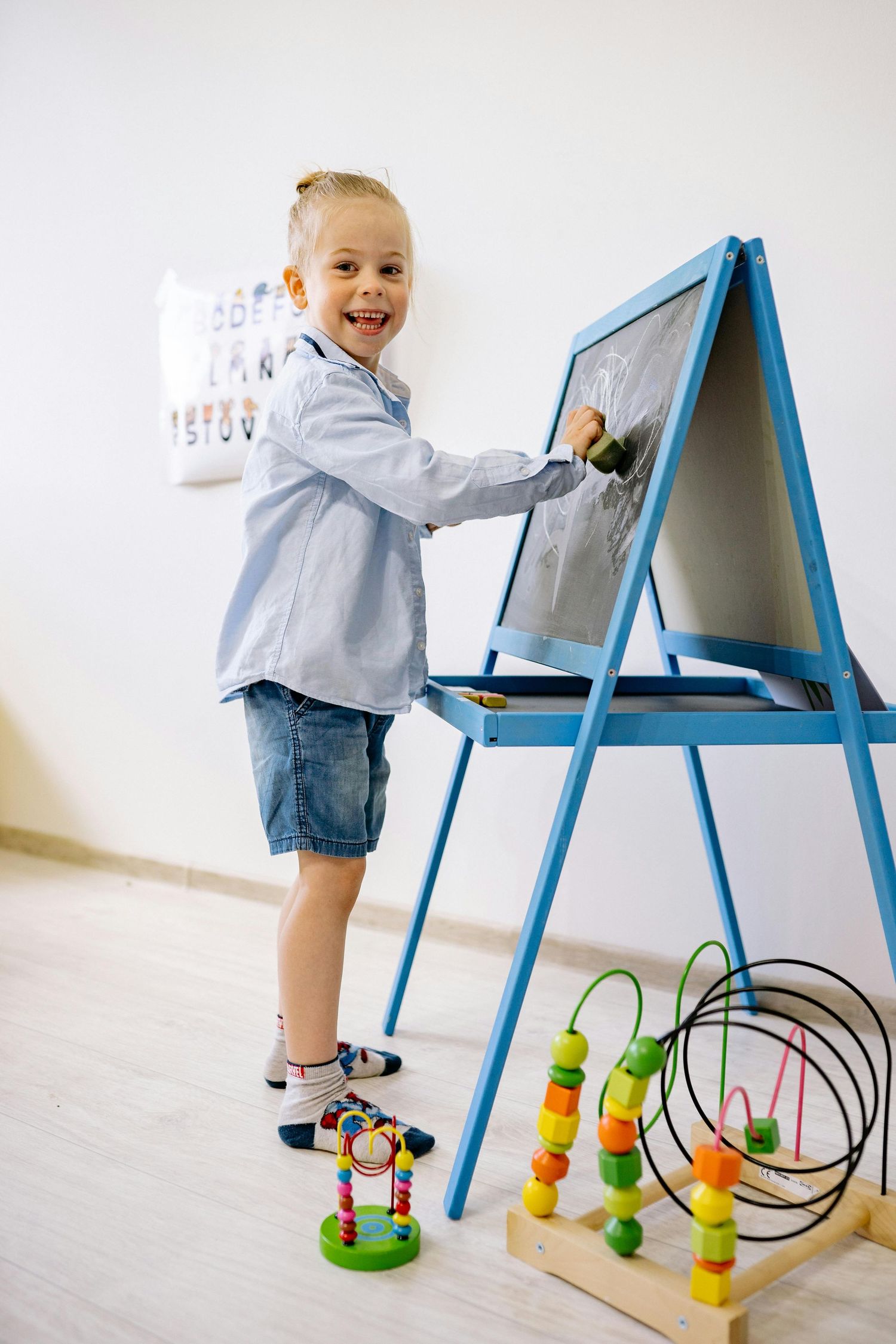Queen Creek  Arizona Daycare Photography Child draws on a blue easel with educational toys and colorful accessories nearby.