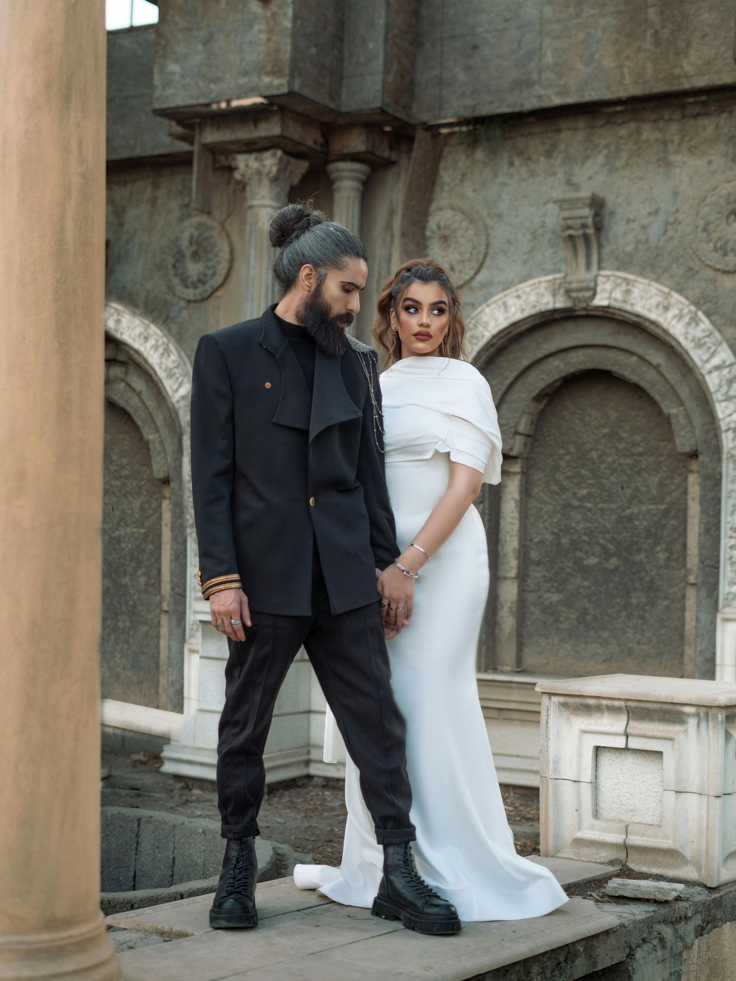 A couple in formal attire poses for artistic wedding photos in a stone colonnade with arched architecture. Trusted Flagstaff Photographer.