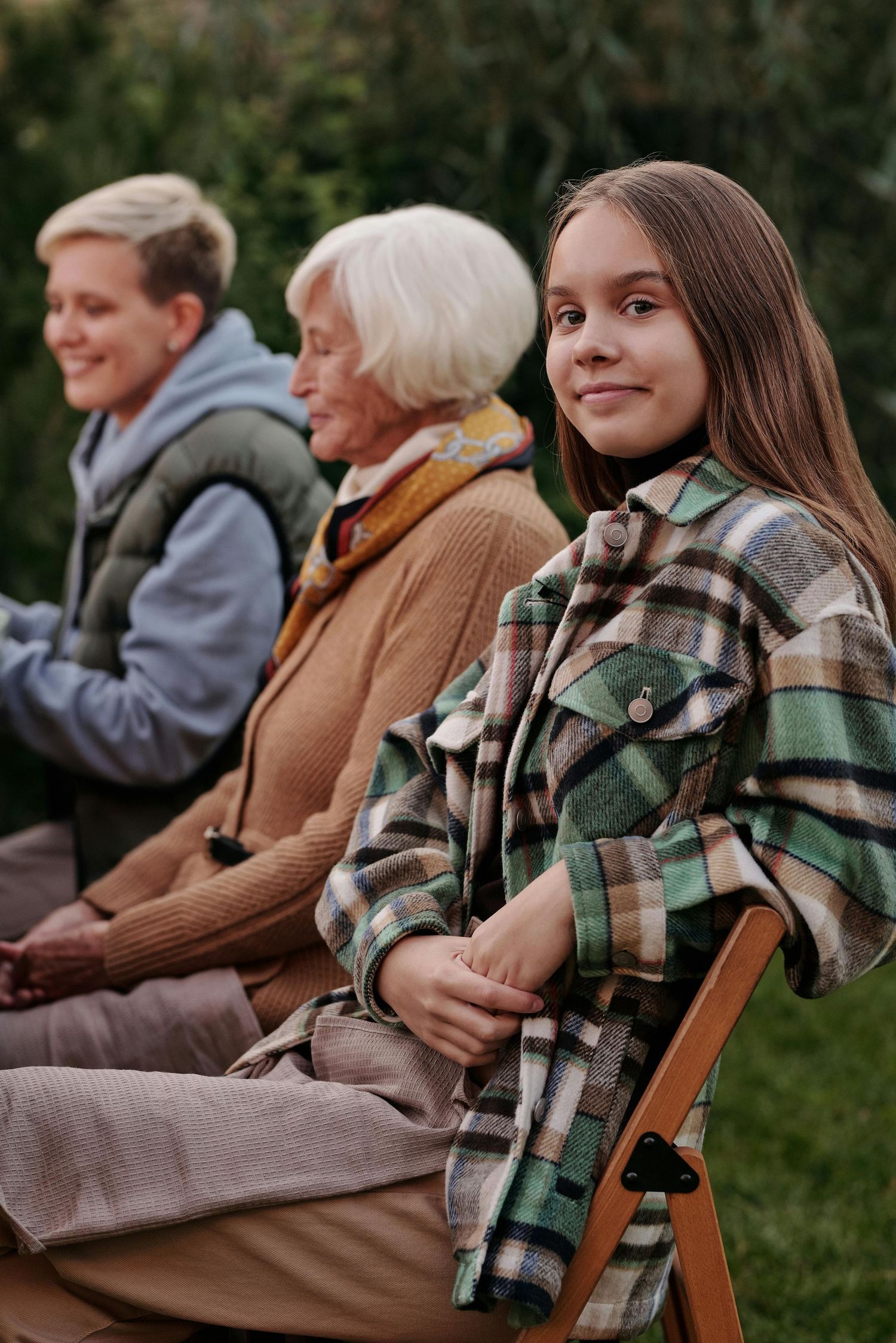 People sitting outdoors on wooden chairs wearing cozy plaid blankets and warm clothing on an autumn evening.
