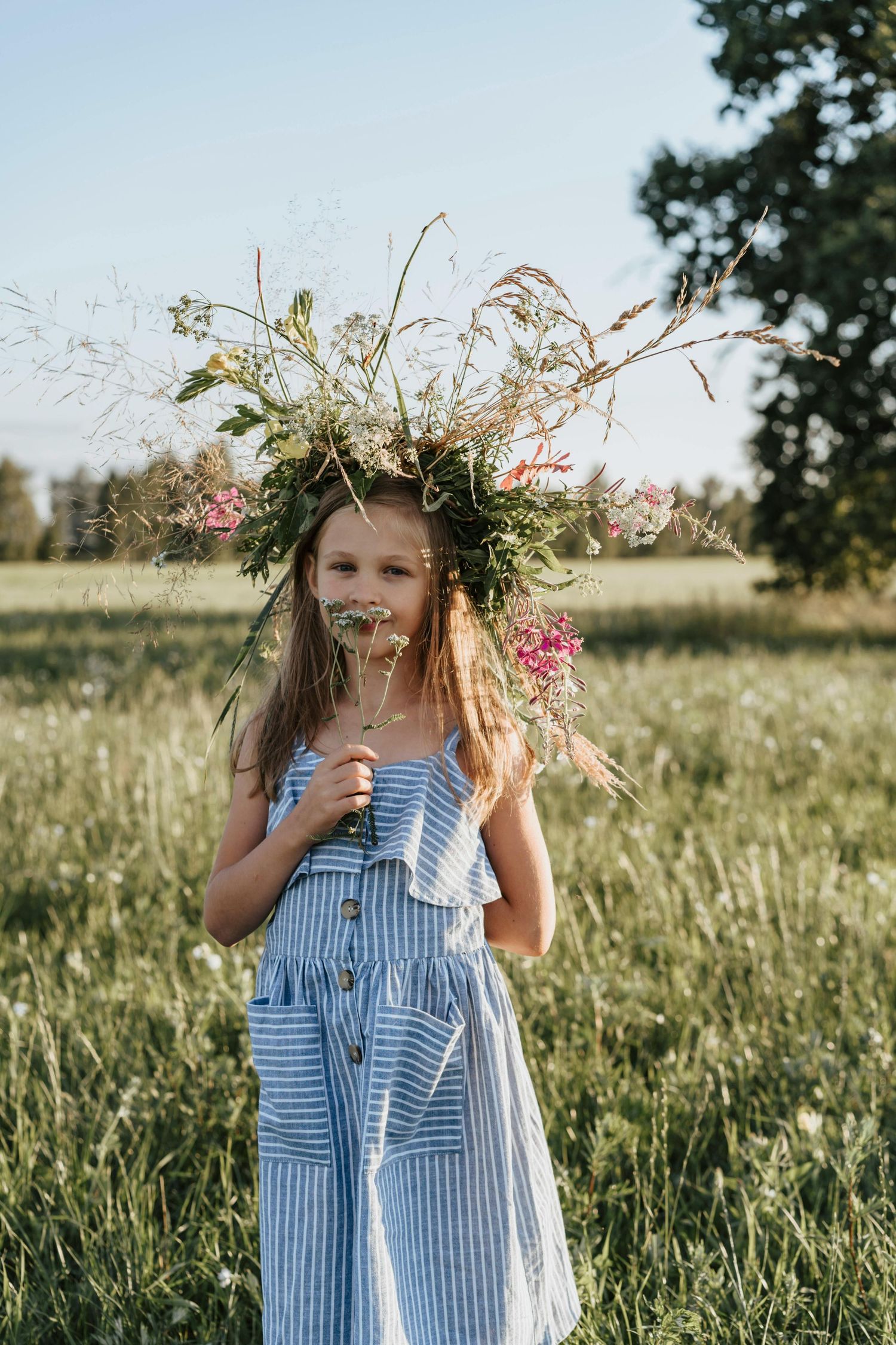 Children's outdoor photography Flagstaff Arizona Someone wearing a blue striped dress poses playfully with wildflowers in a summer meadow.