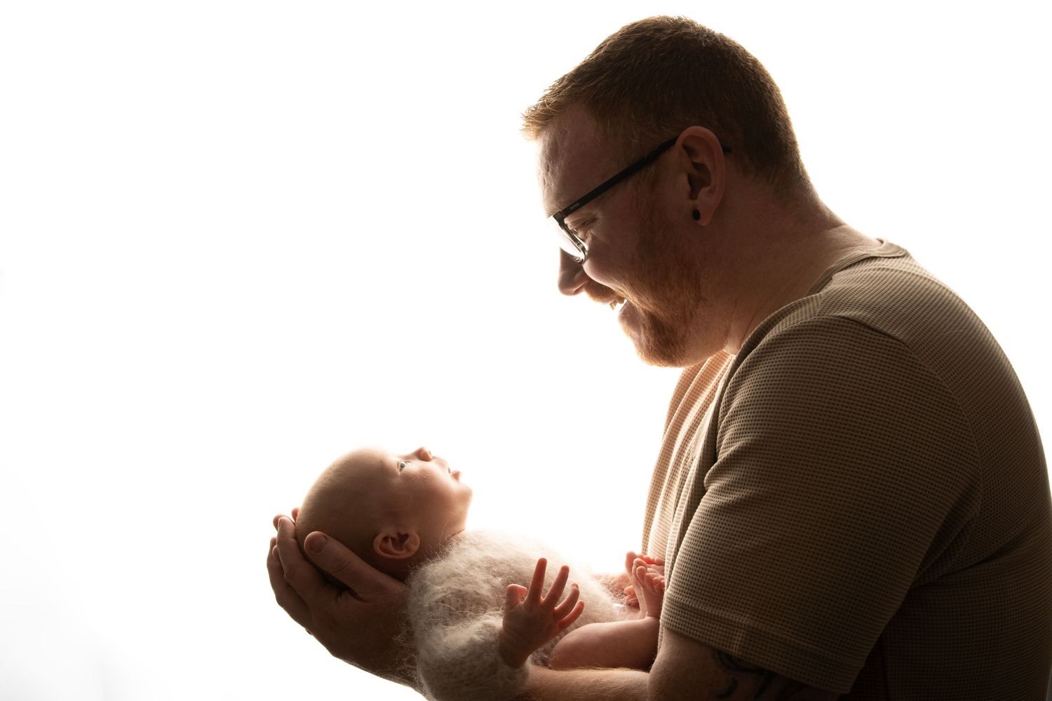 Newborn photography image of father holding little baby framed by light