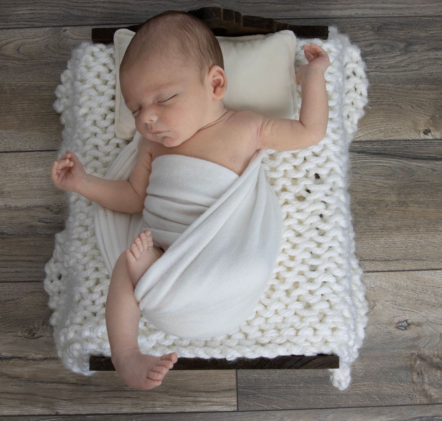 Newborn baby posed on a little wooden bed with cream blanket in photography session
