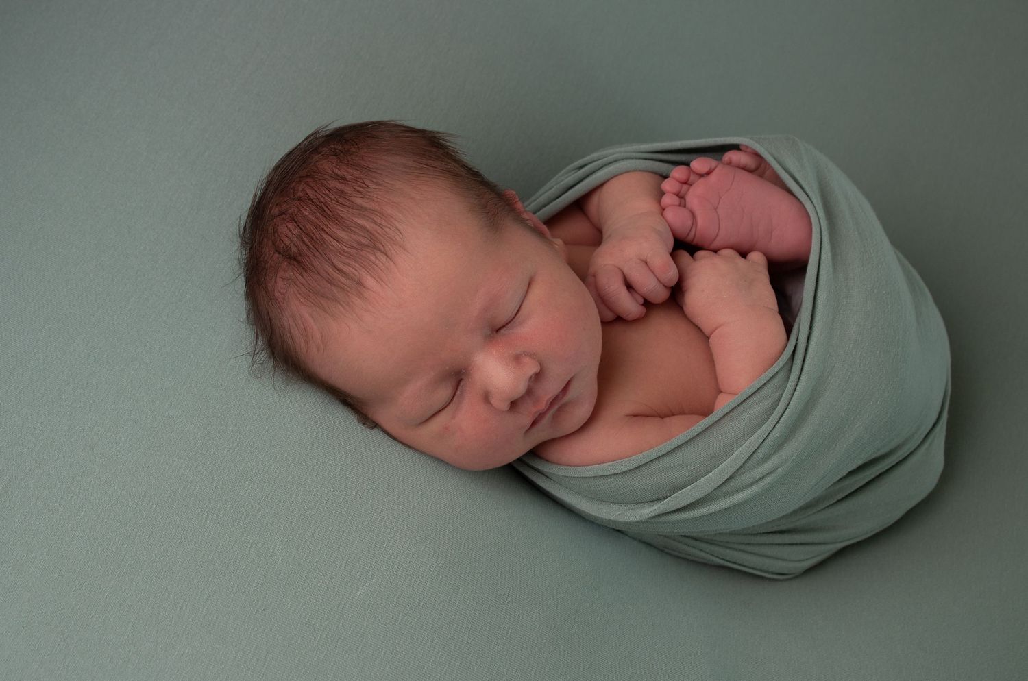 Little baby all tucked up in a green wrap for newborn photography session