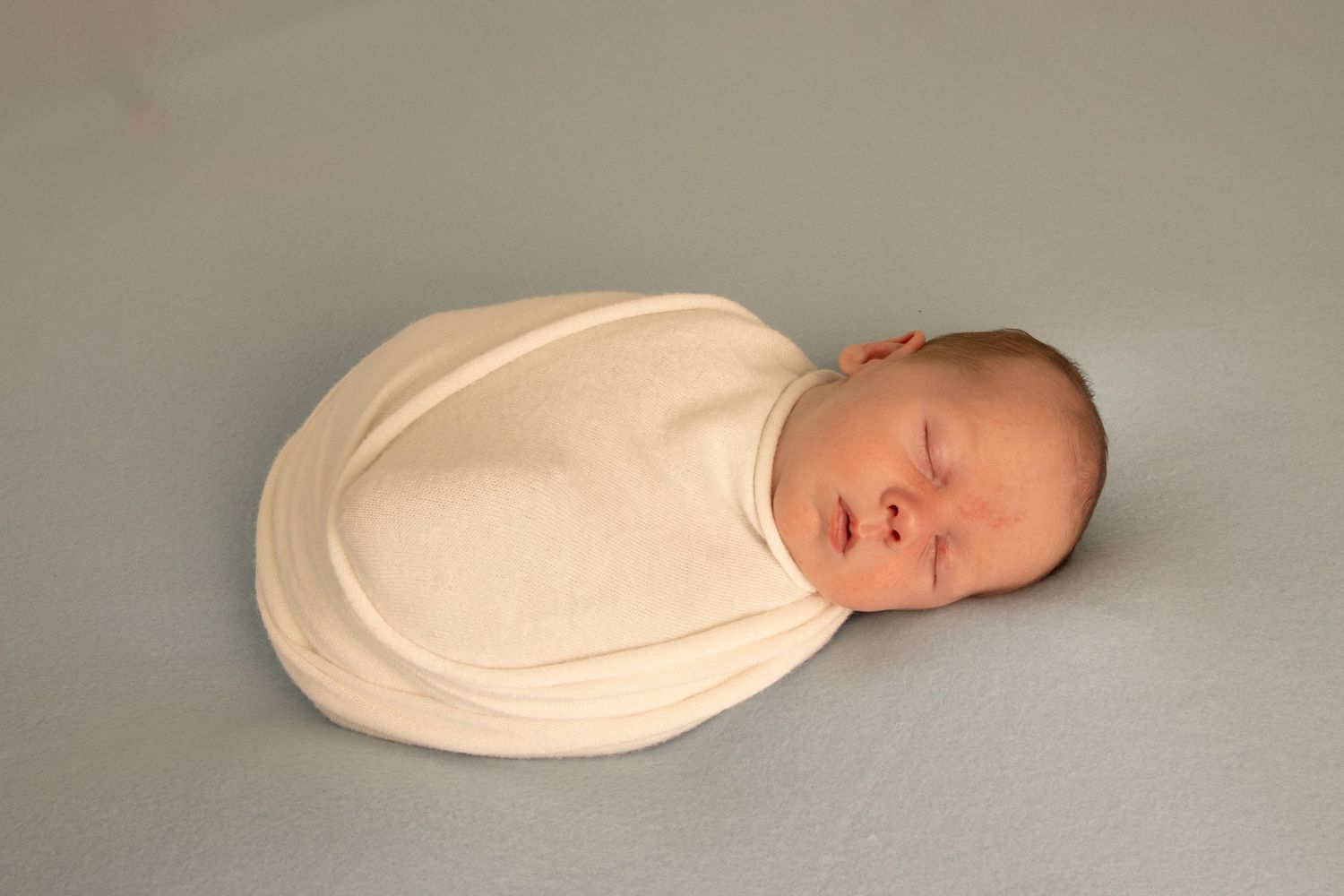 Sleeping newborn baby in a cream wrap on blue blanket