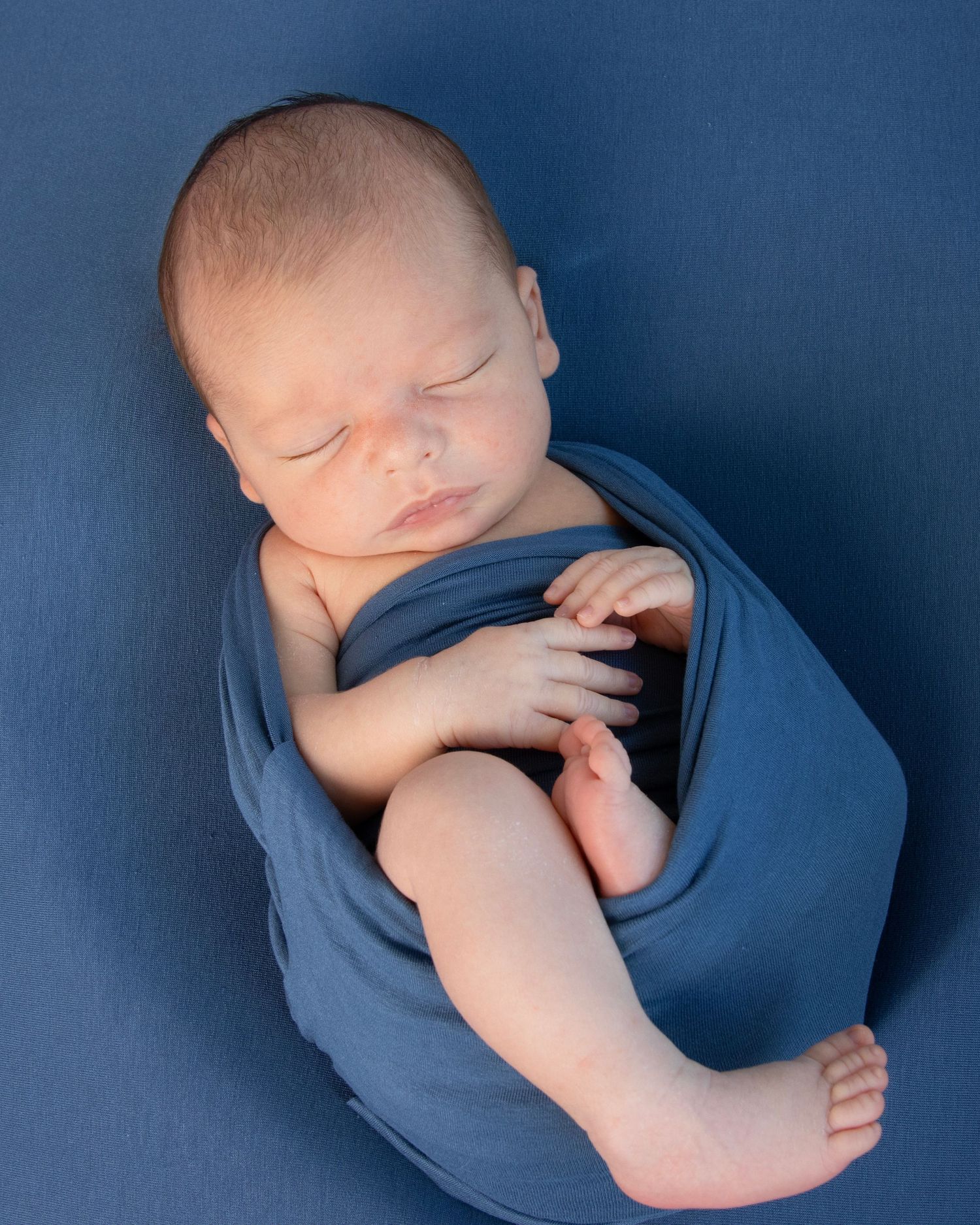 Baby wrapped in a blue wrap in newborn portrait session