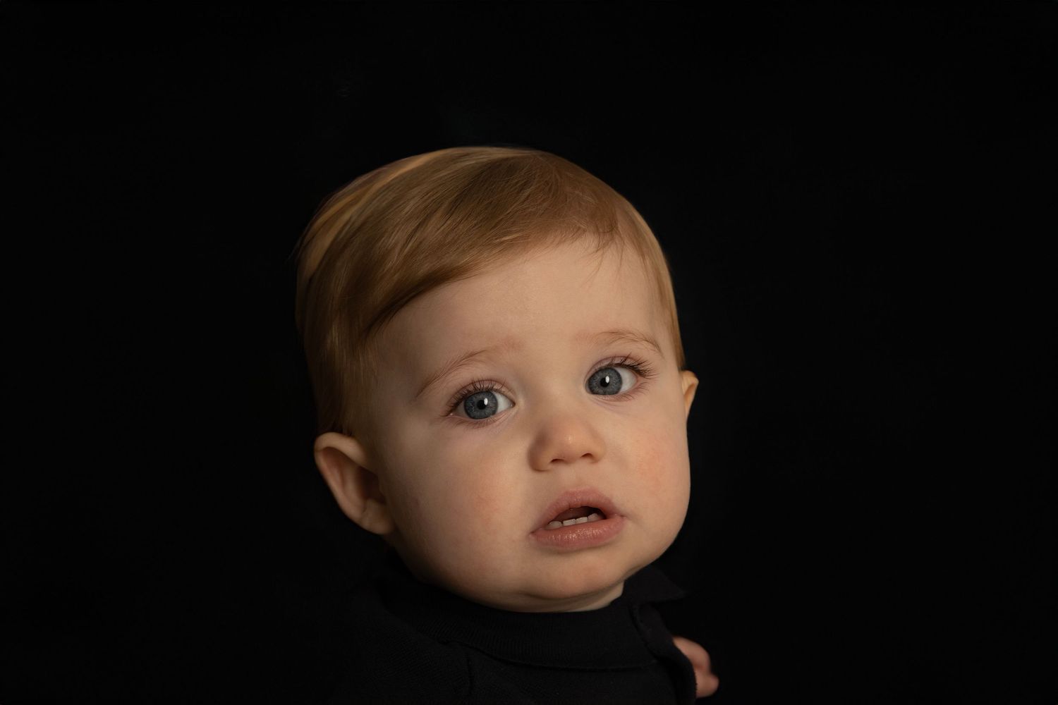 Portrait of a baby with blue eyes against a black background.