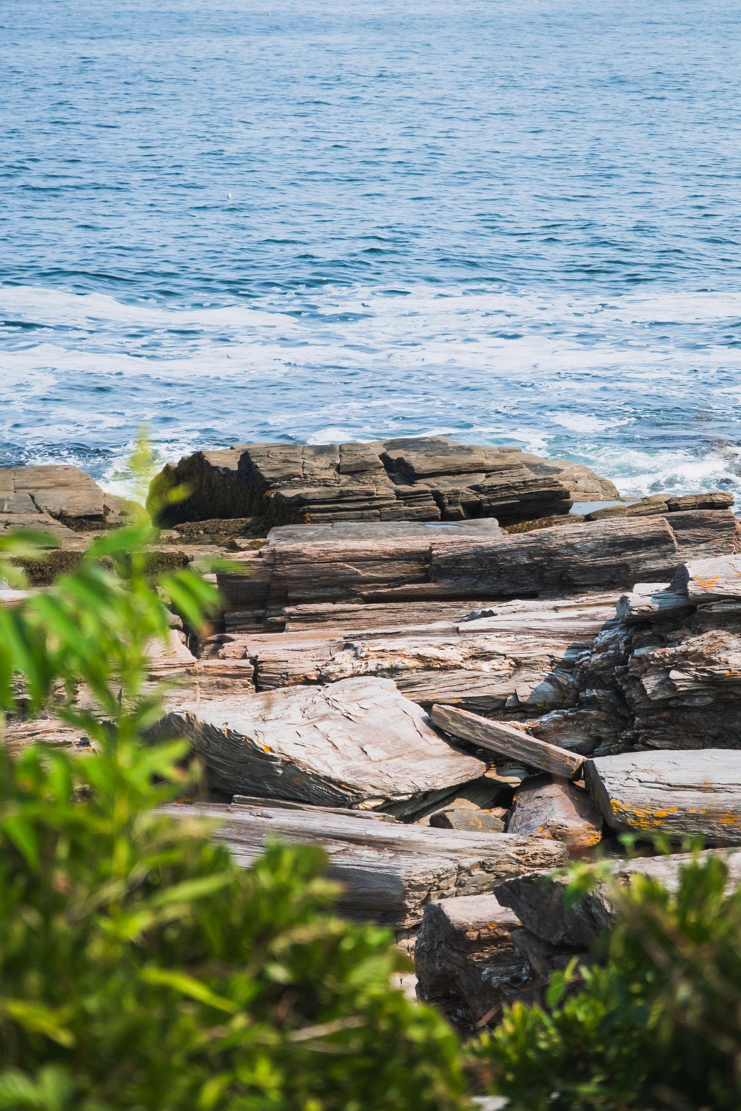 Rocky coastal outcrop with layered stone formations against blue ocean waters.