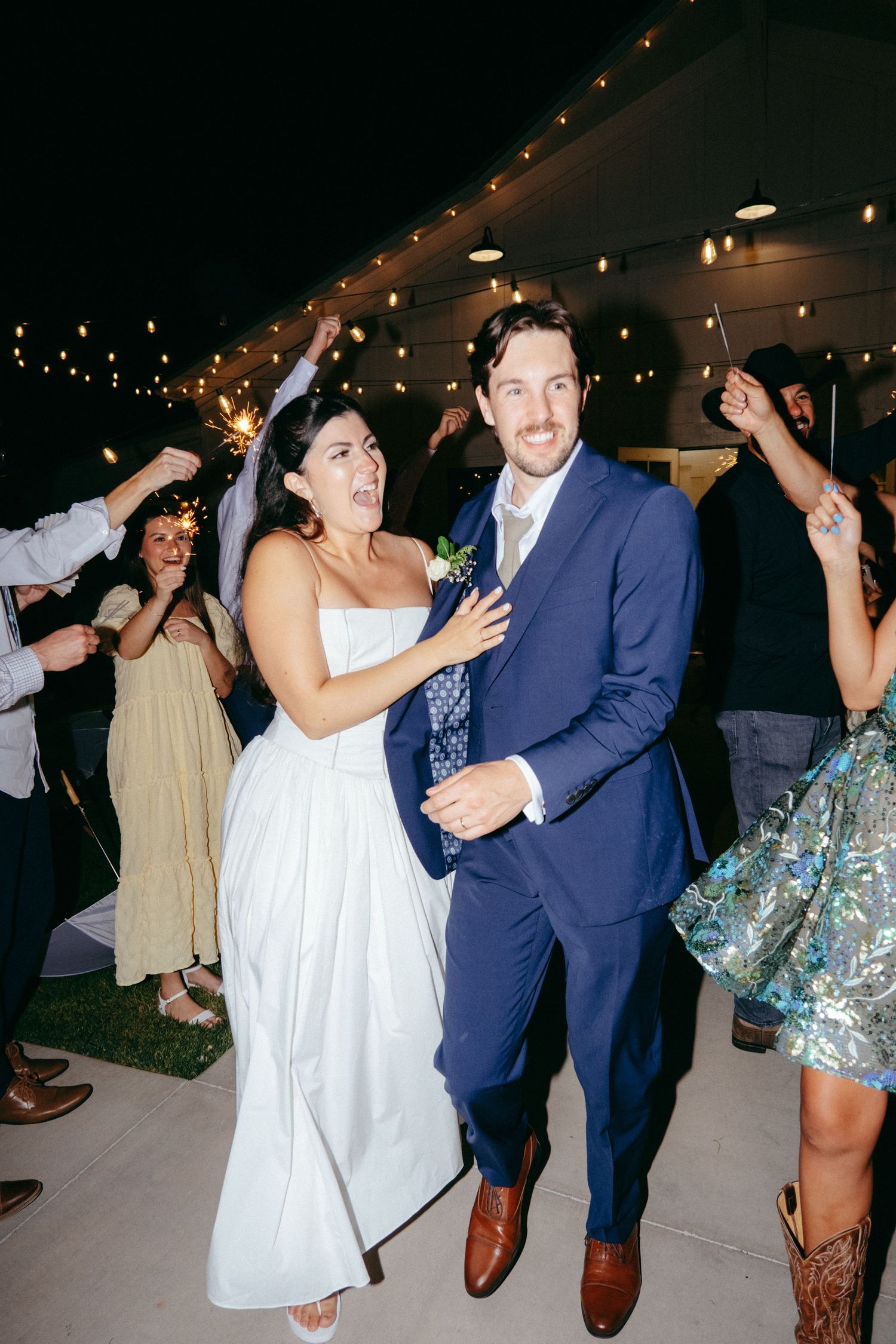 Wedding guests dancing and celebrating at an evening reception under string lights.