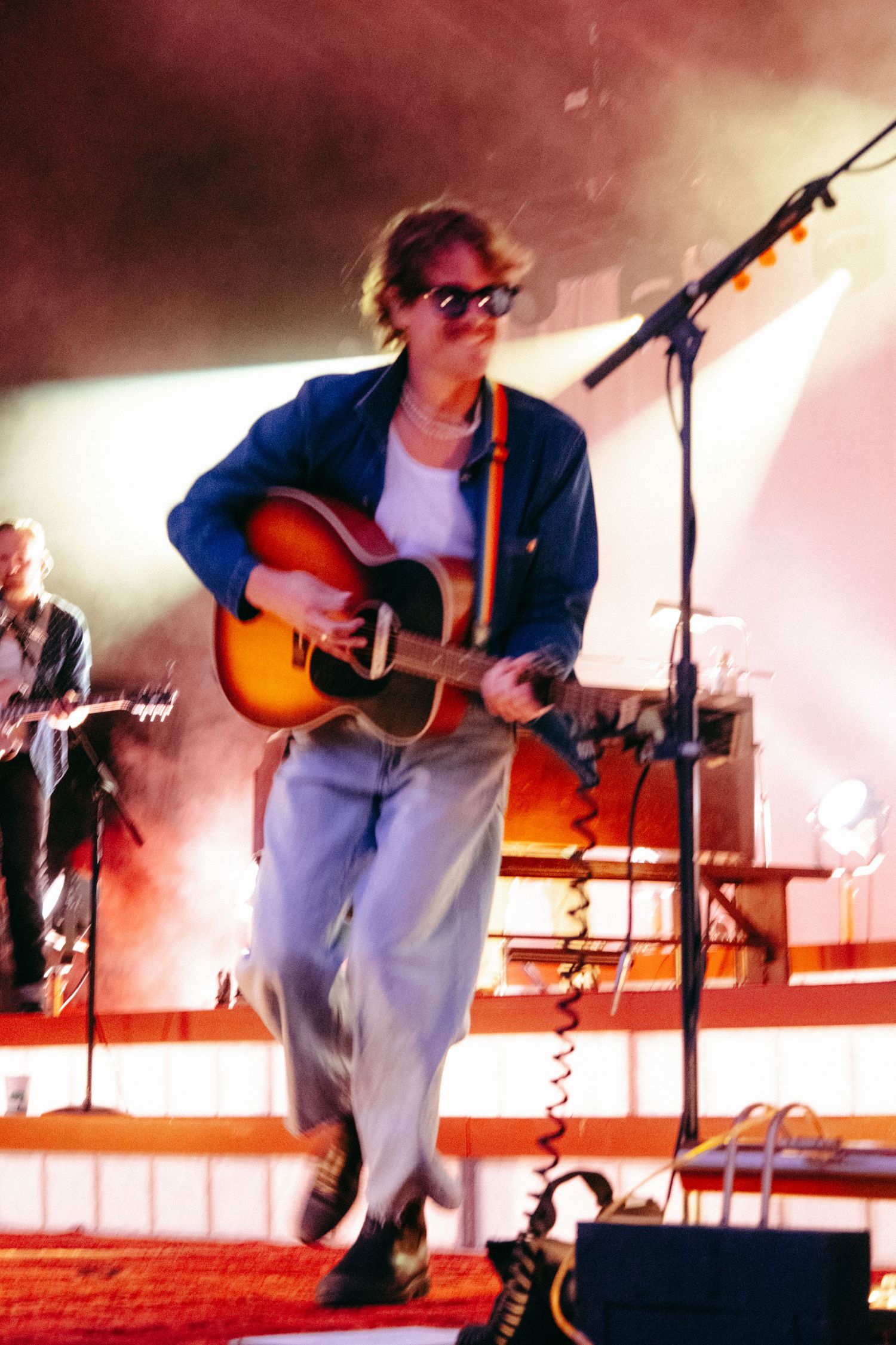 Performer playing guitar on stage with red and white lighting effects.