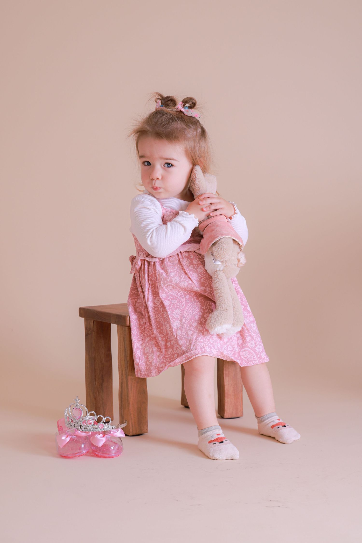 Studio portrait featuring pink dress and wooden bench against neutral background.