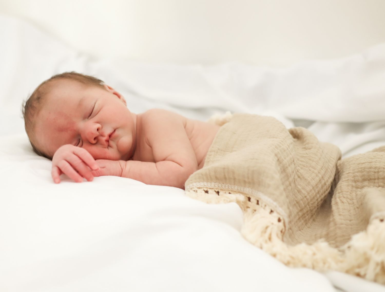 Sleeping newborn wrapped in cream colored blanket on white background.