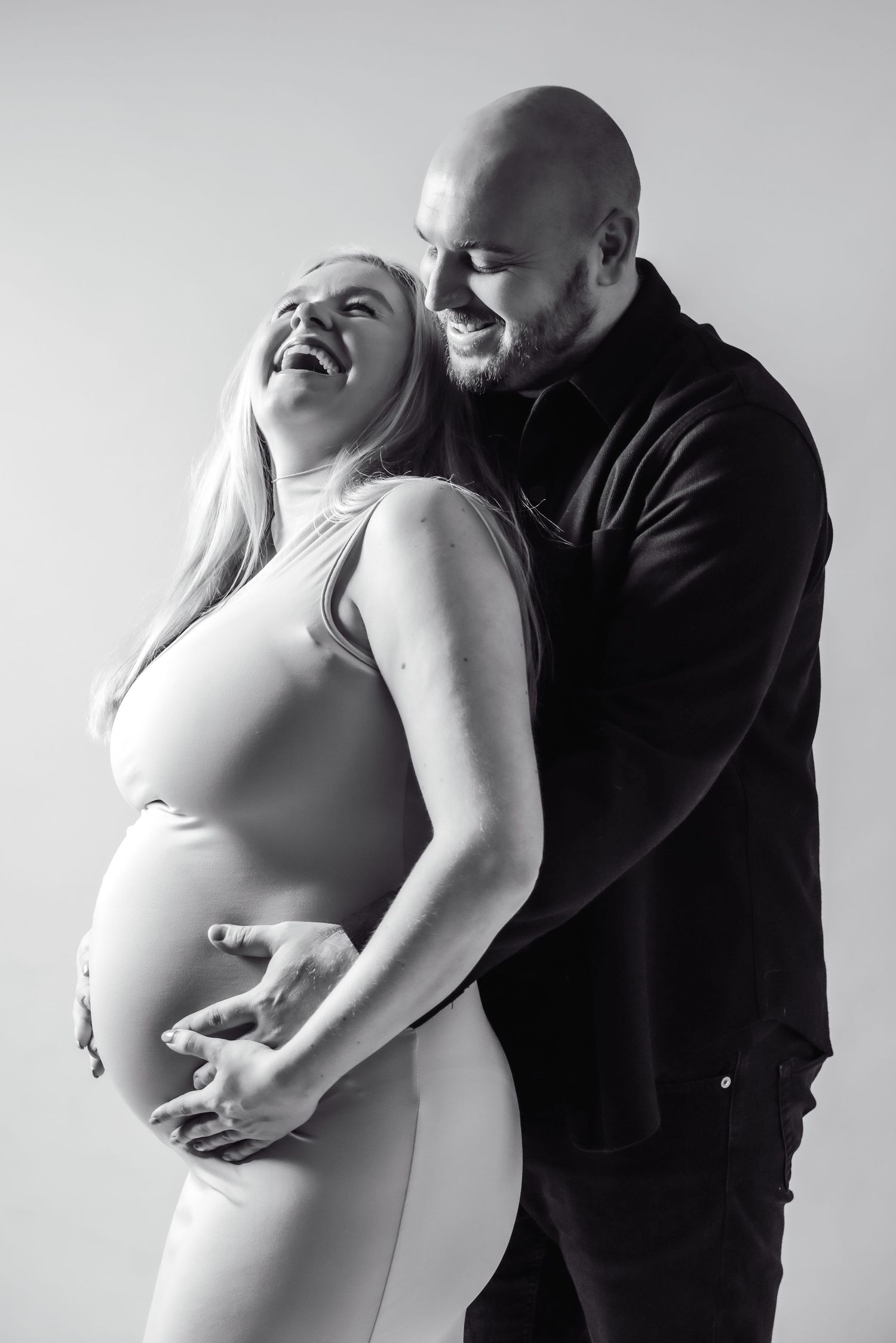 A series of black and white maternity photos showing a couple embracing and laughing together.