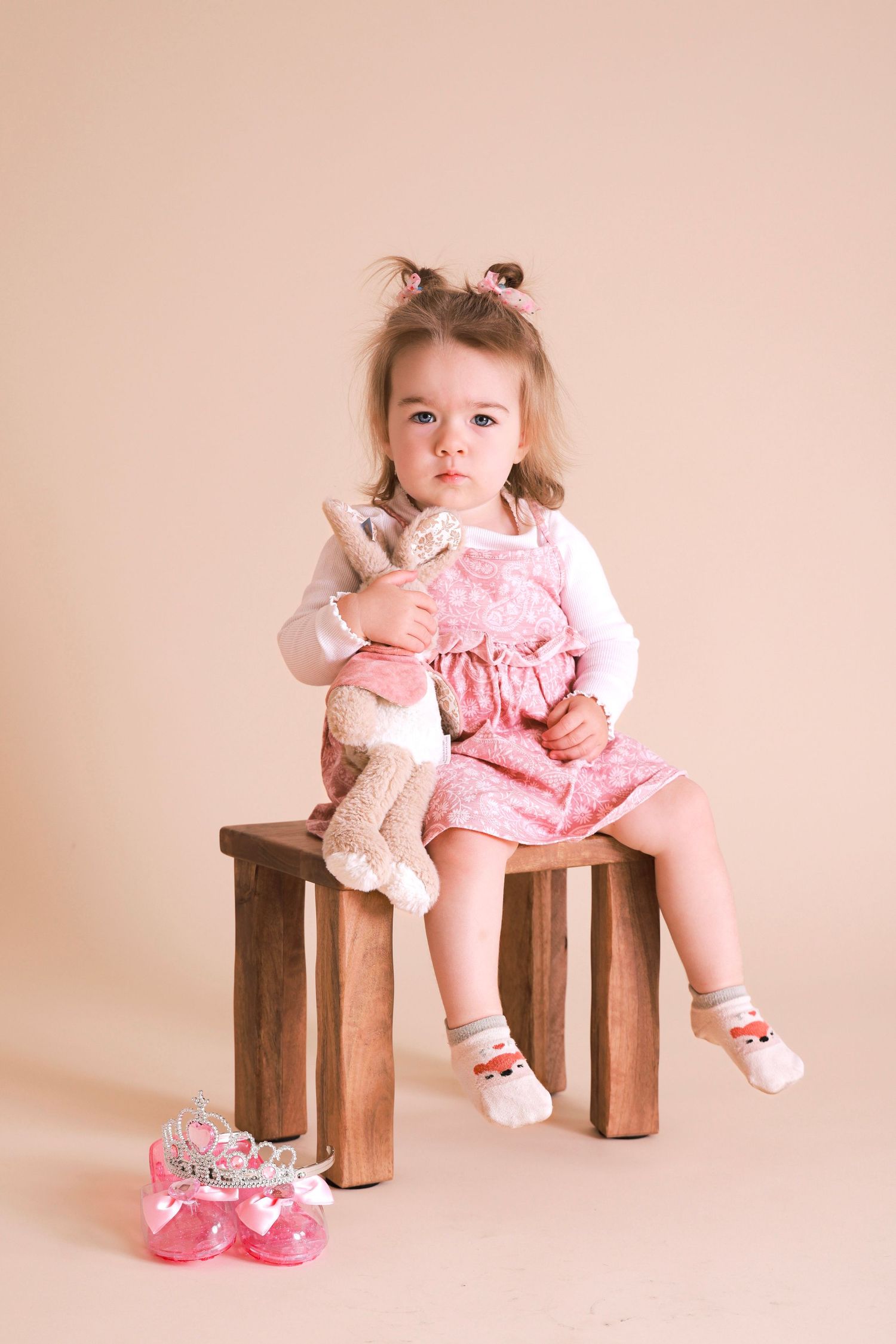 Portrait session with wooden bench prop and pink dress against peachy backdrop.