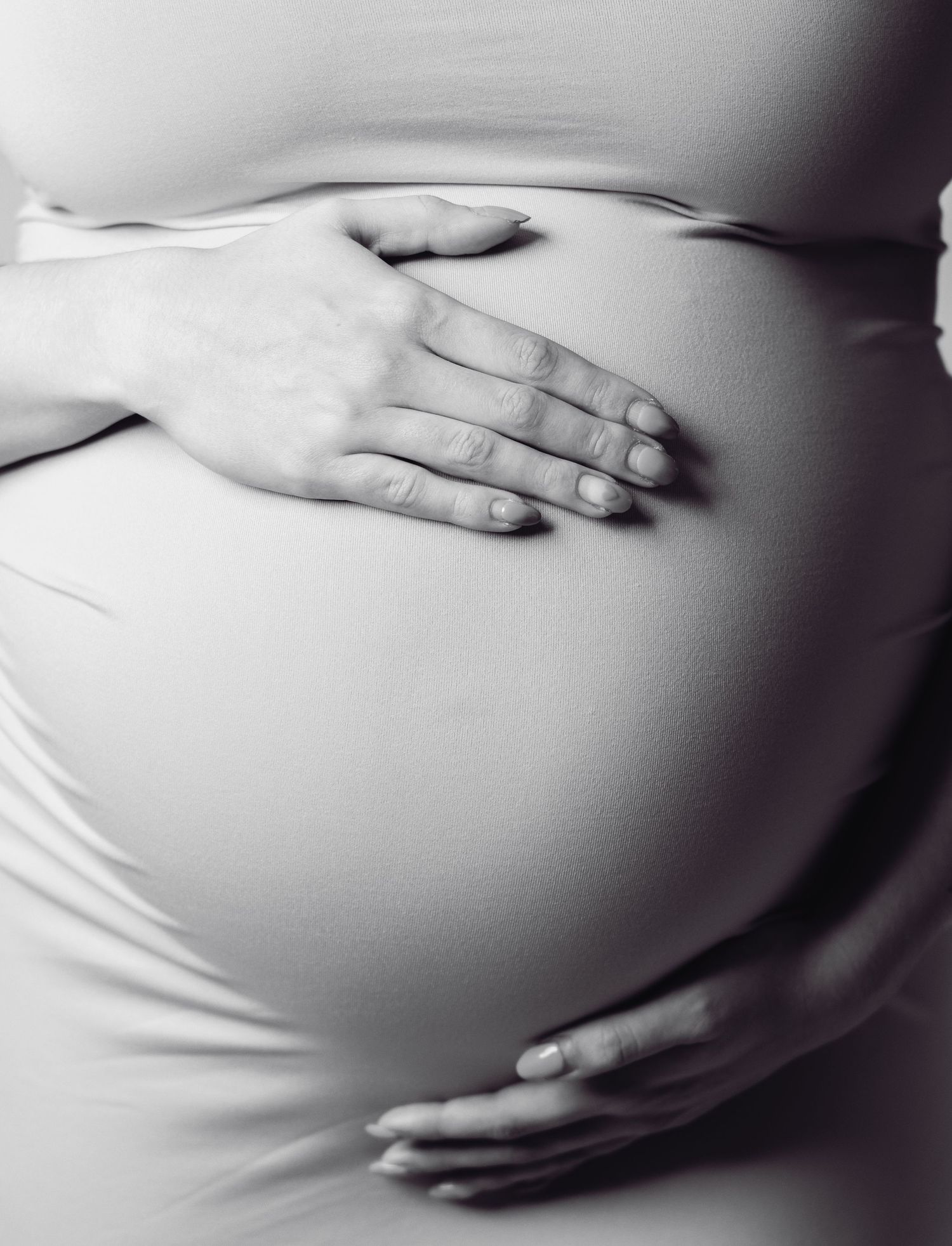 Black and white photo of hands gently cradling a pregnant belly covered in white fabric.