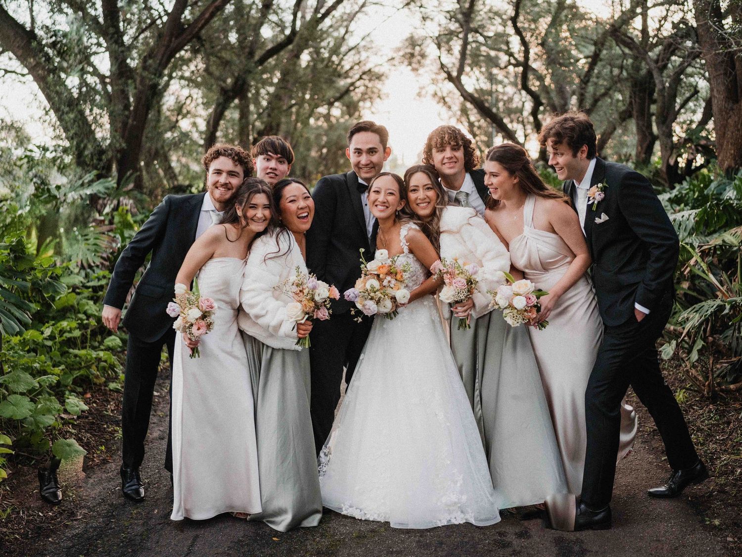 Wedding party poses together outdoors in formal attire against natural backdrop.
